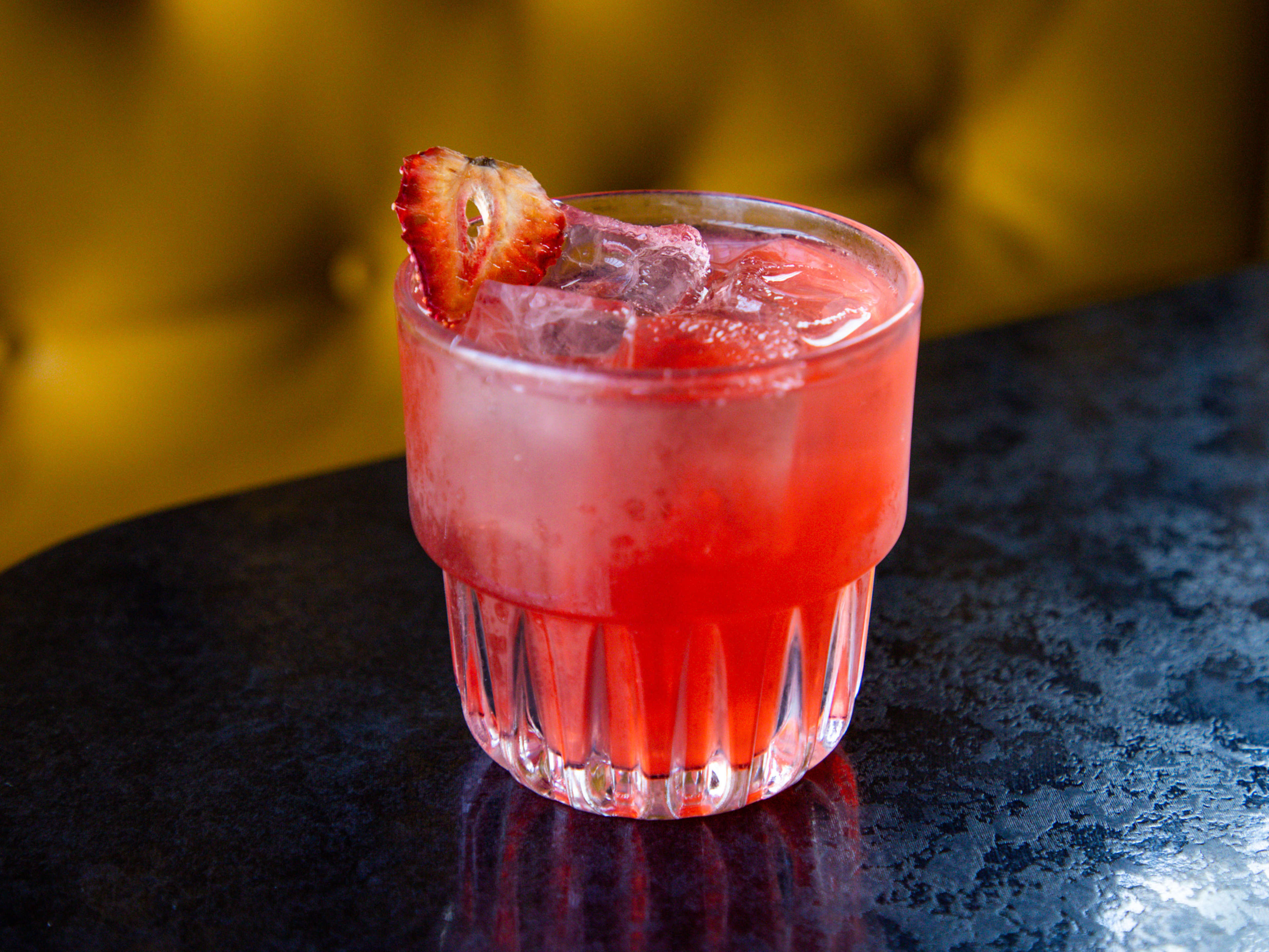 a deep-pink colored clarified strawberry margarita cocktail on a table at Nickel CIty