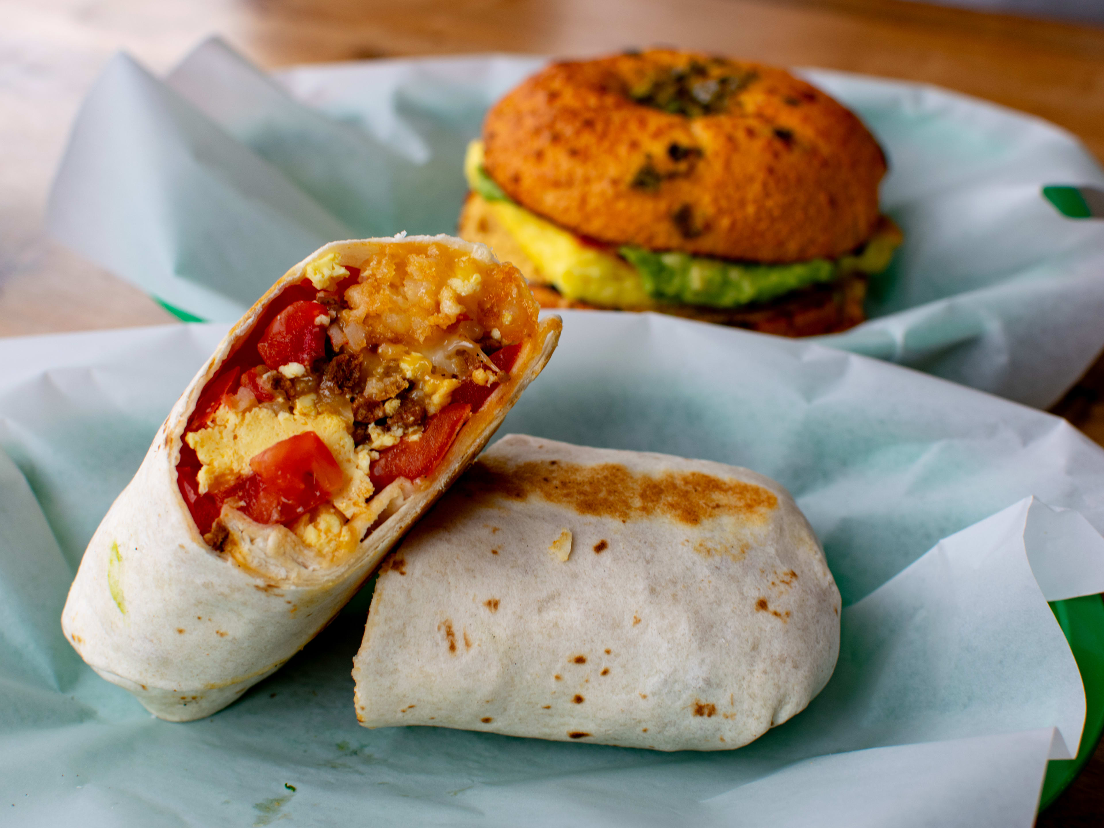 A breakfast burrito and breakfast sandwich on paper-lined trays.