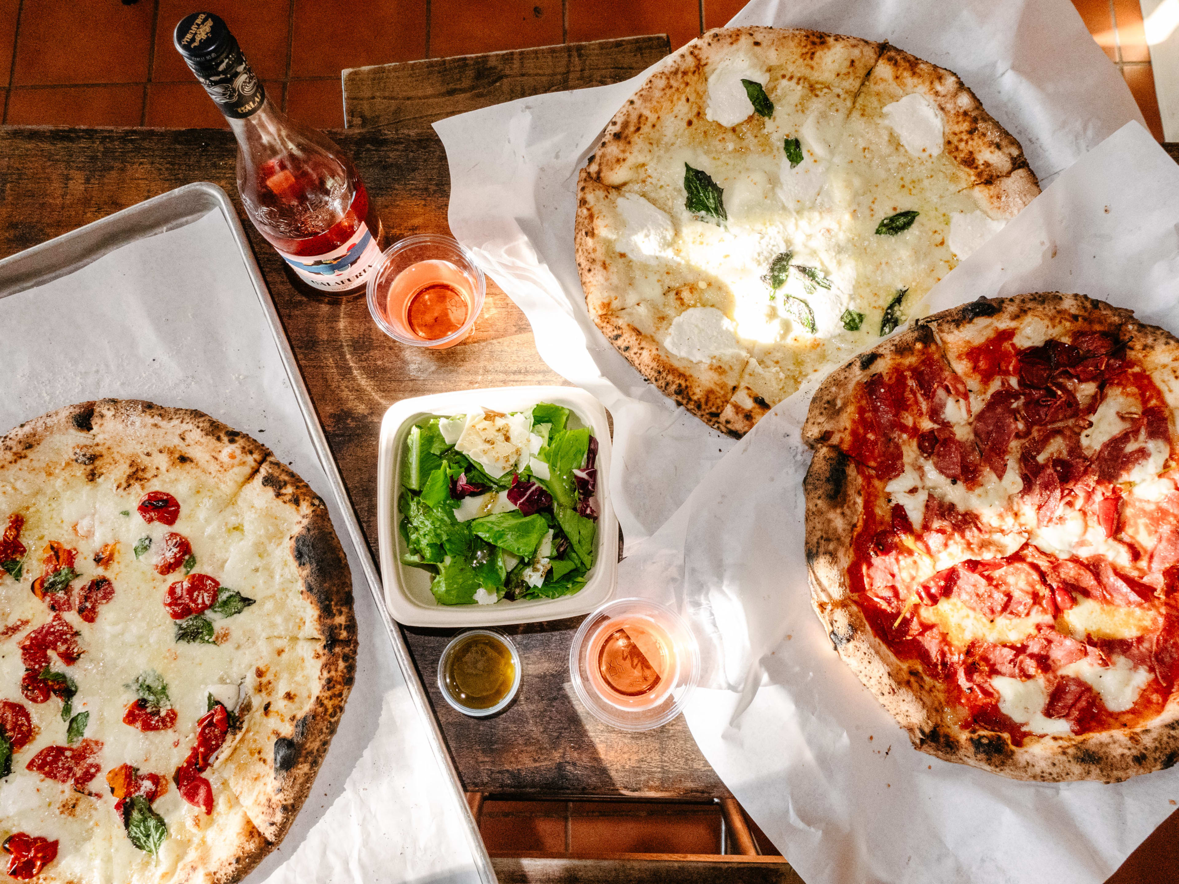 Three pizza's on a table with a salad in between them.