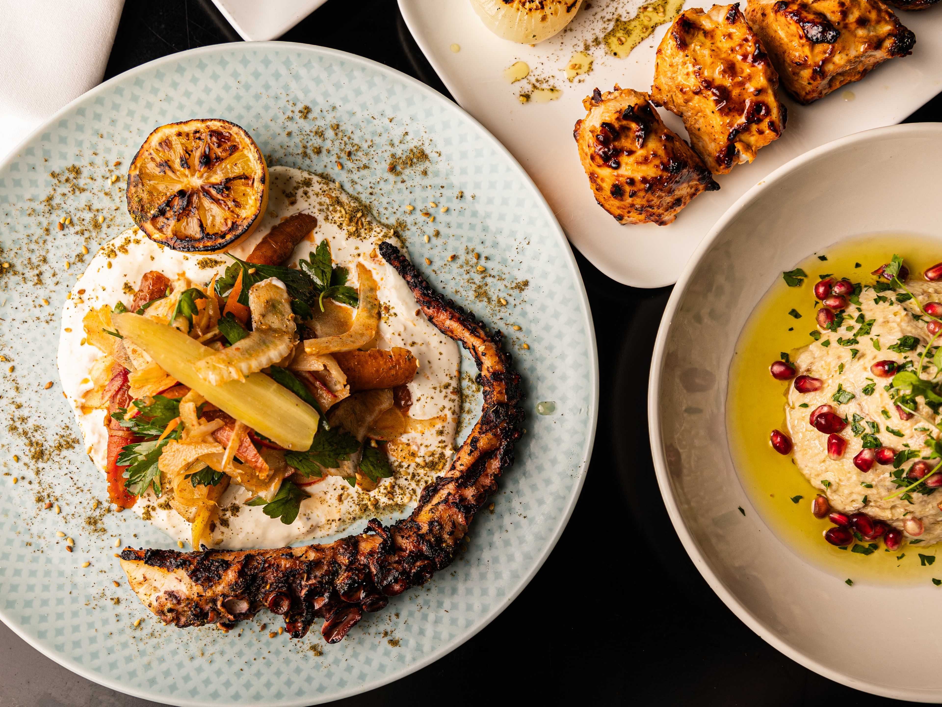 Vegetables, hummus, chick peas, octopus on a light blue plate.