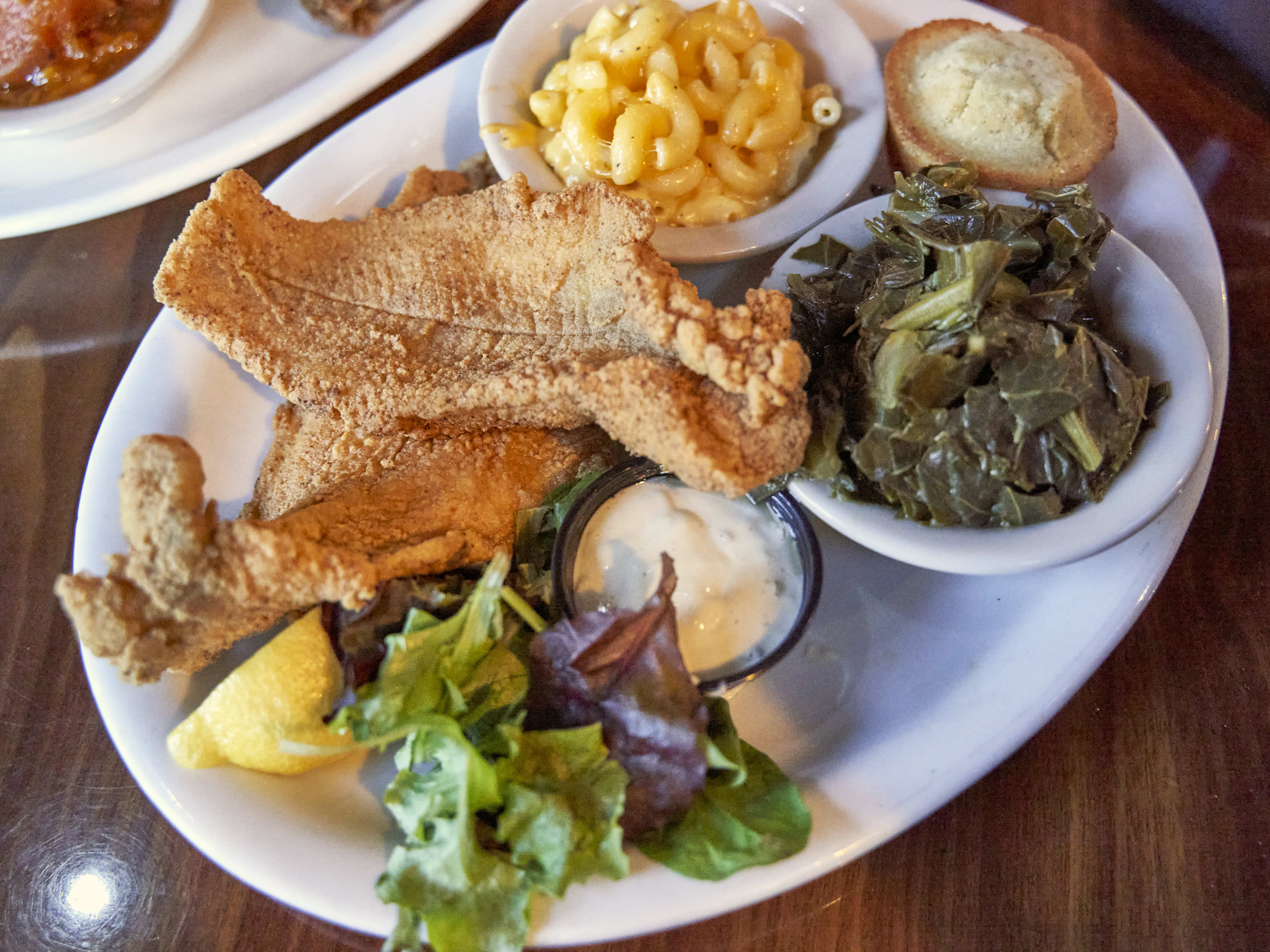 Fried fish, greens, mac&cheese, and corn muffin on a white plate.