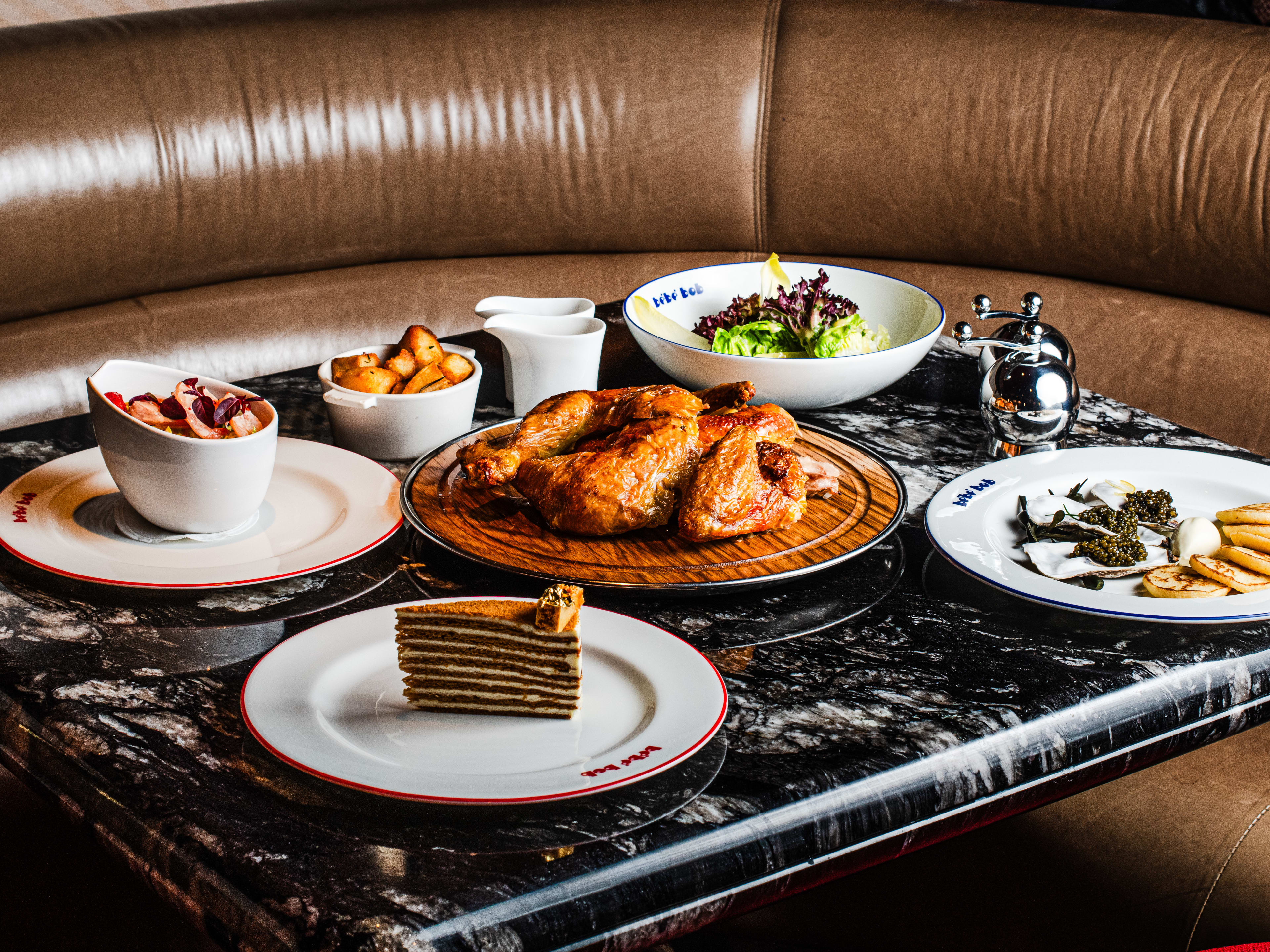 A spread of dishes on a marble table around a leather booth.