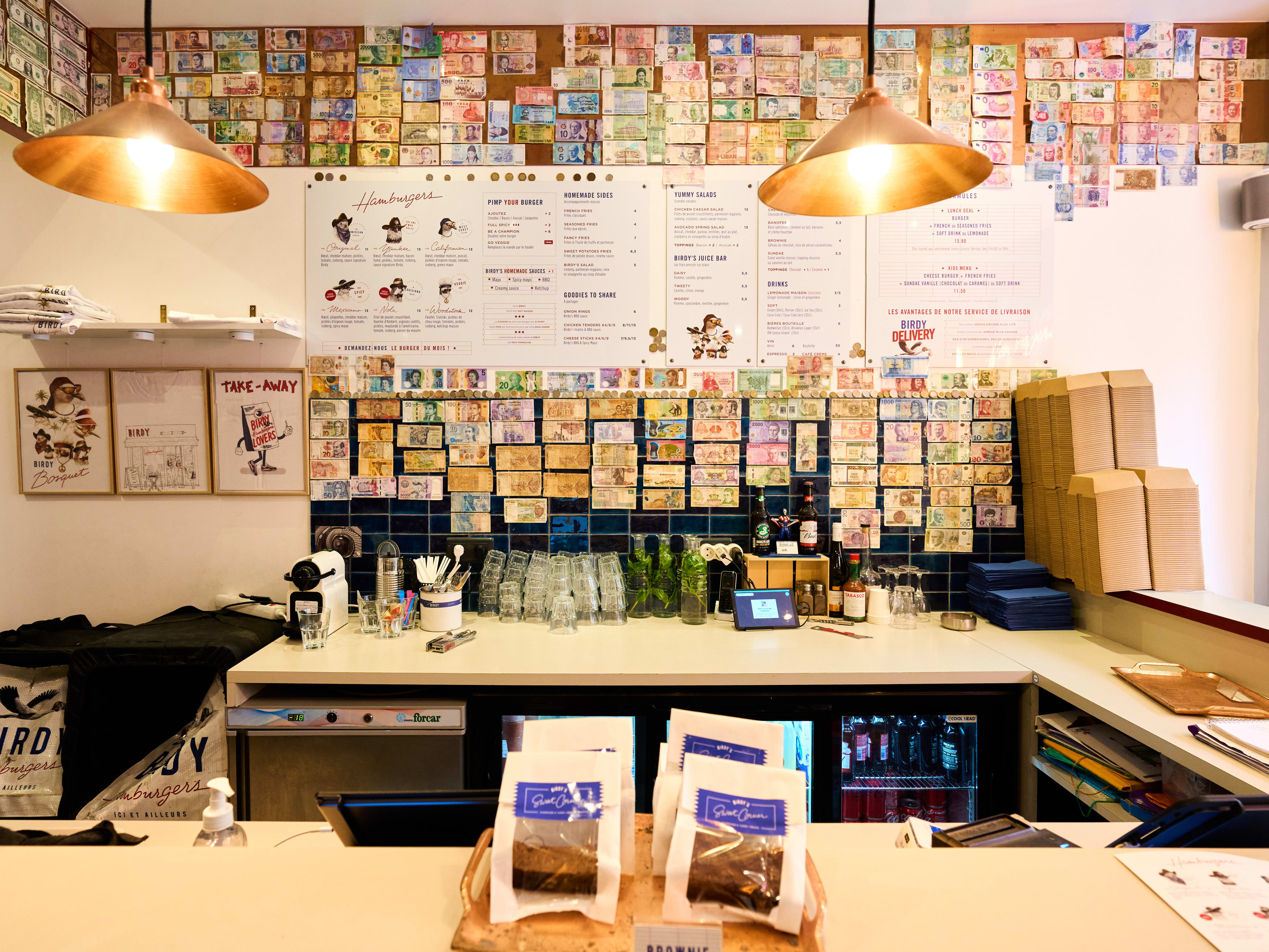 Burger counter with lots of international bills on walls at Birdy