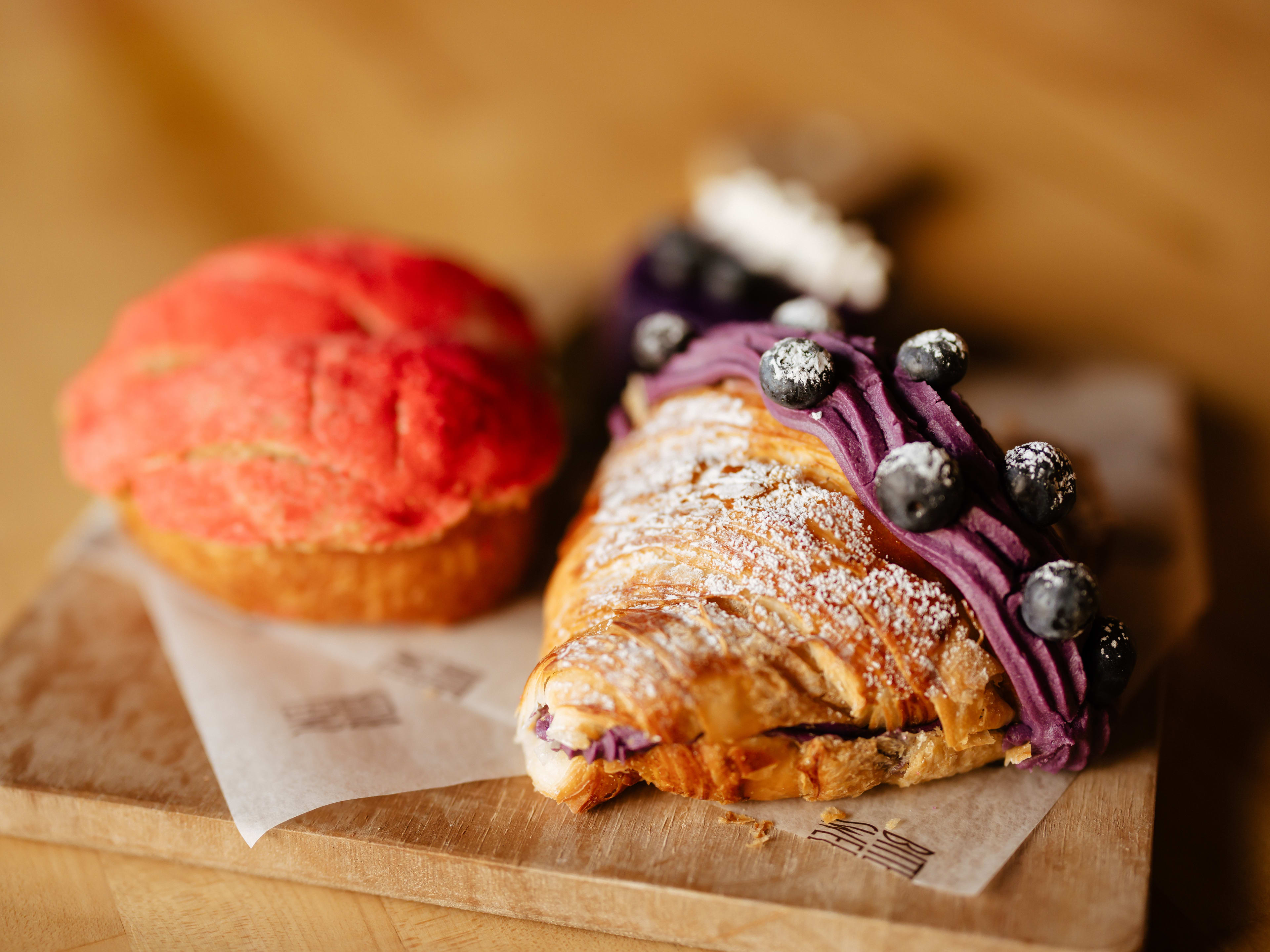 A heart-shaped ube croissant and other pastries sitting on a wooden board