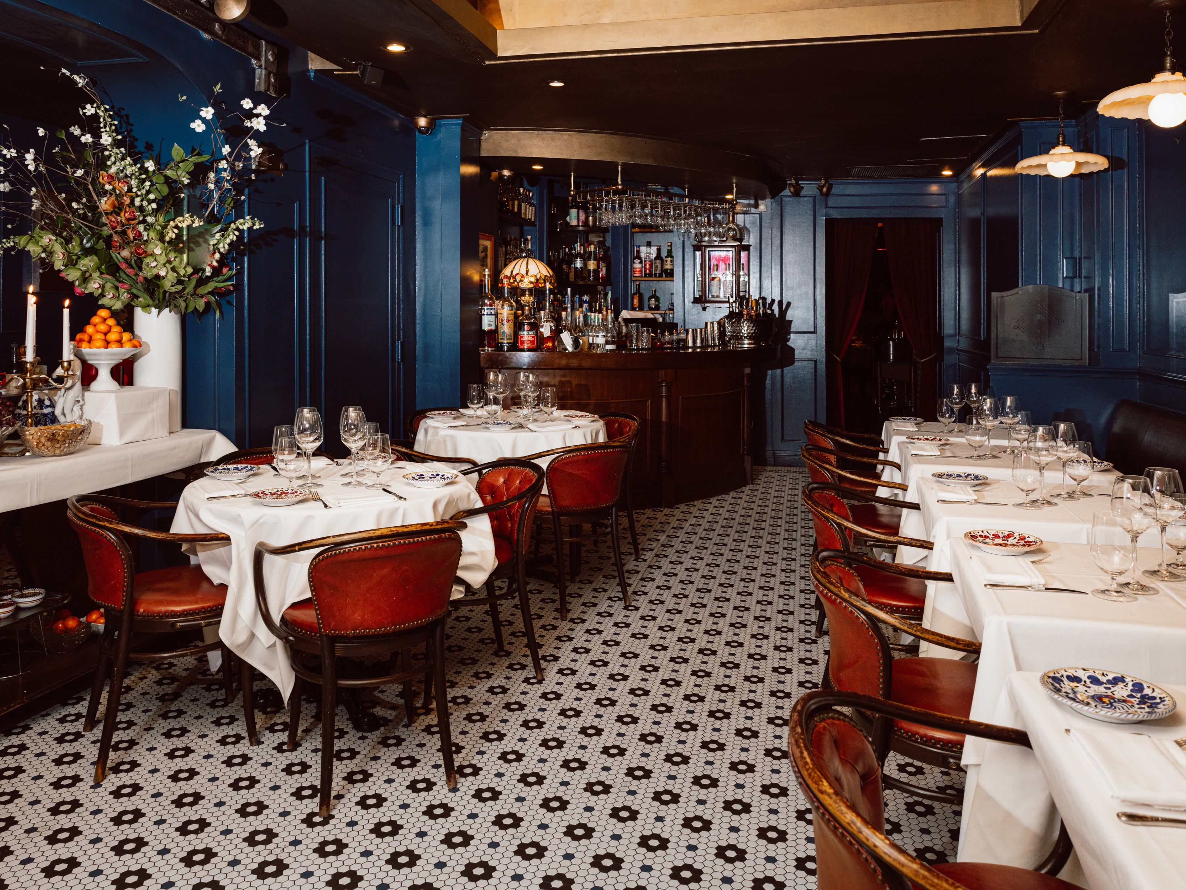 The blue interior of Carbone with tables with white tablecloths and large paintings.