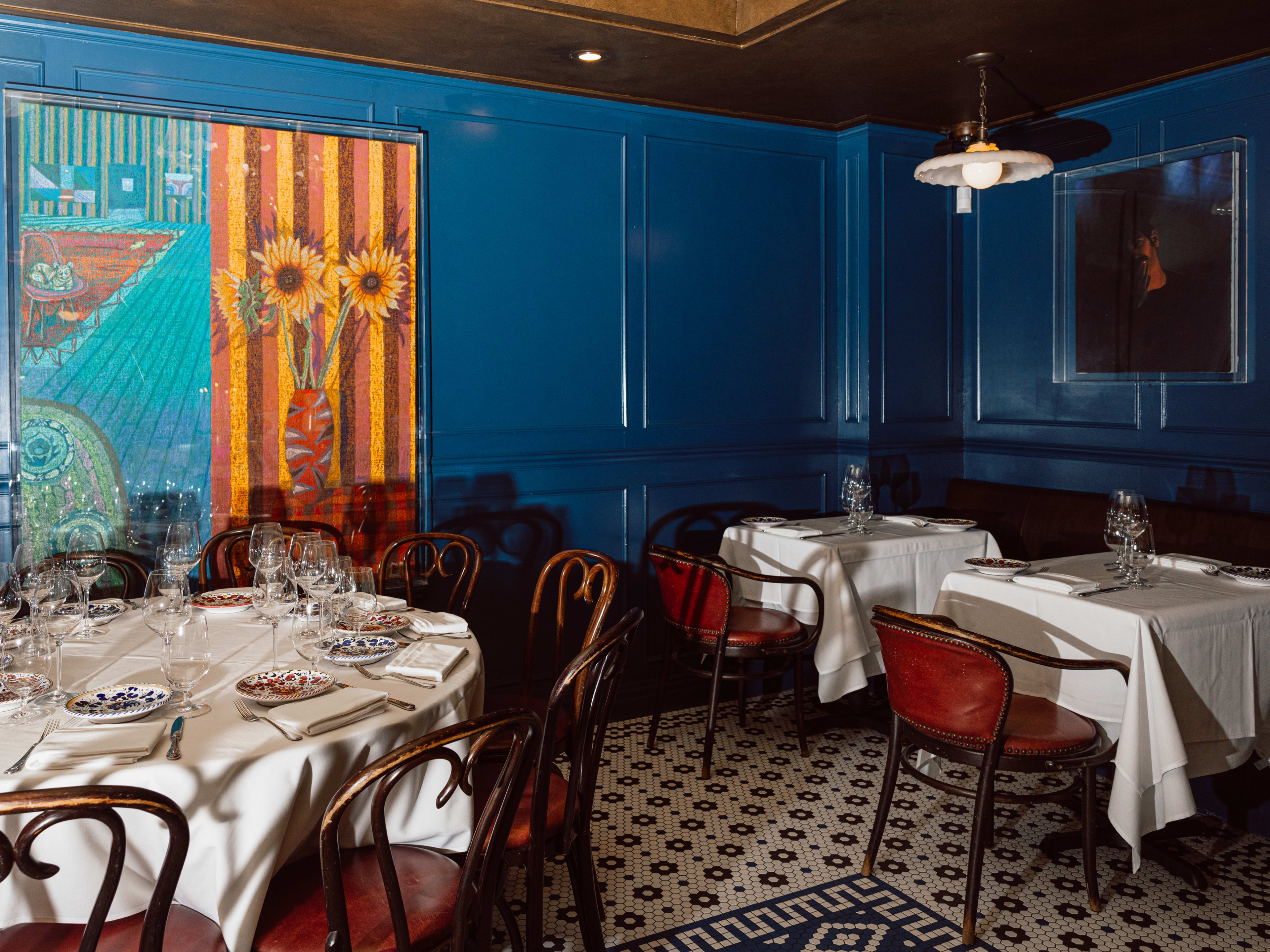 The blue interior of Carbone with tables with white tablecloths and large paintings.