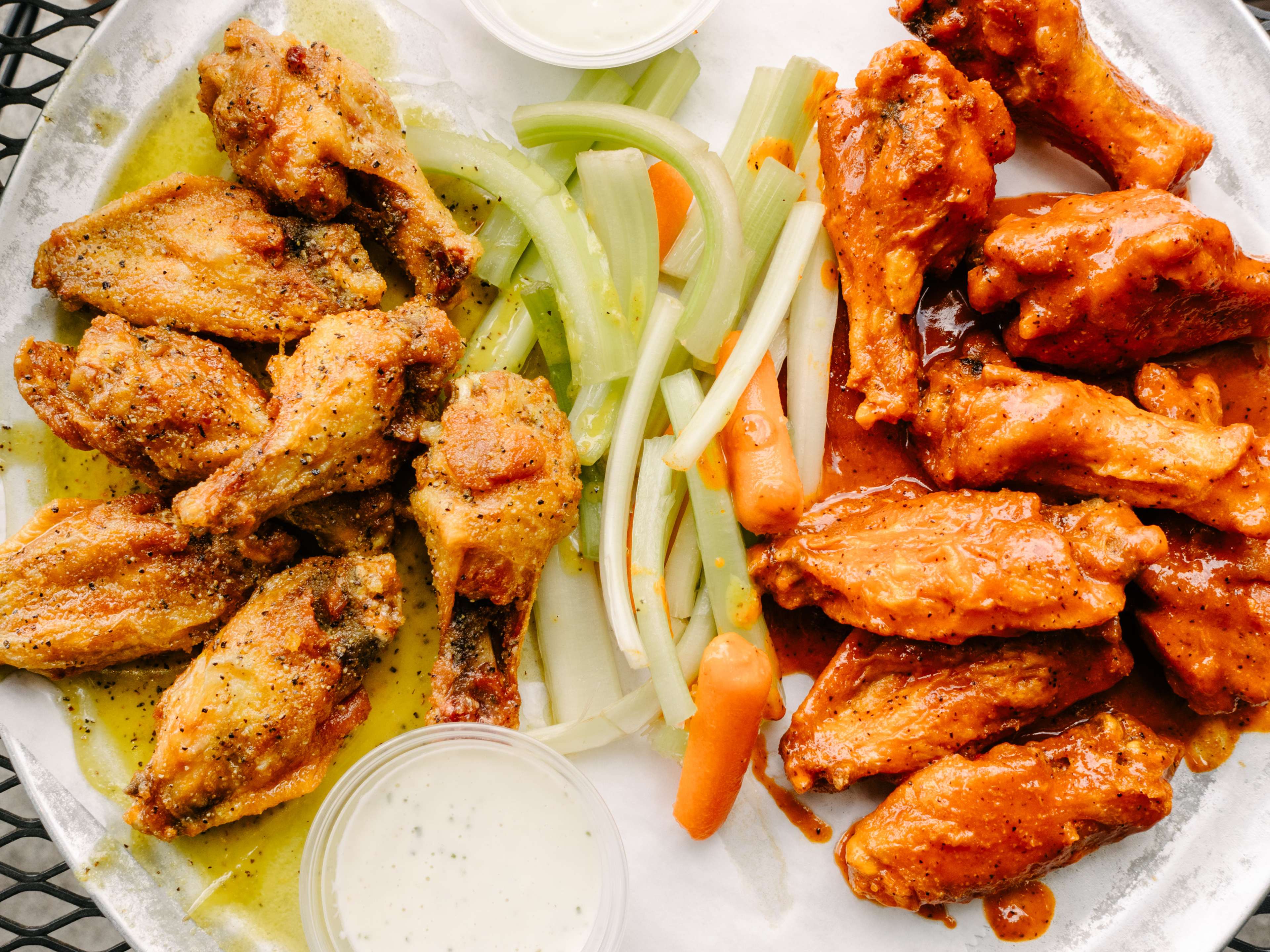 Buffalo wings and lemon pepper wings with celery and carrots between them.