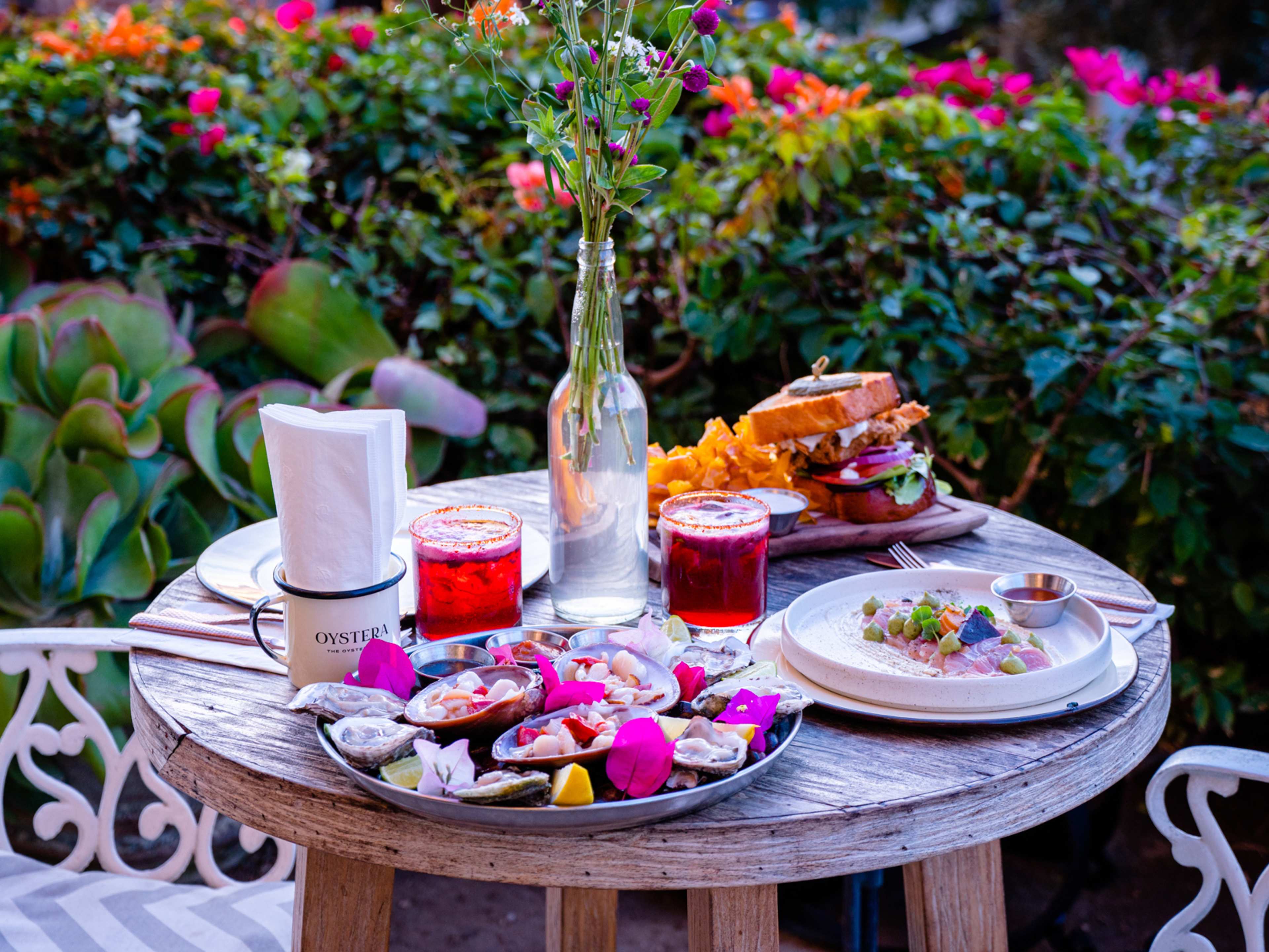 Spread of food and cocktails on outdoor table at Oystera