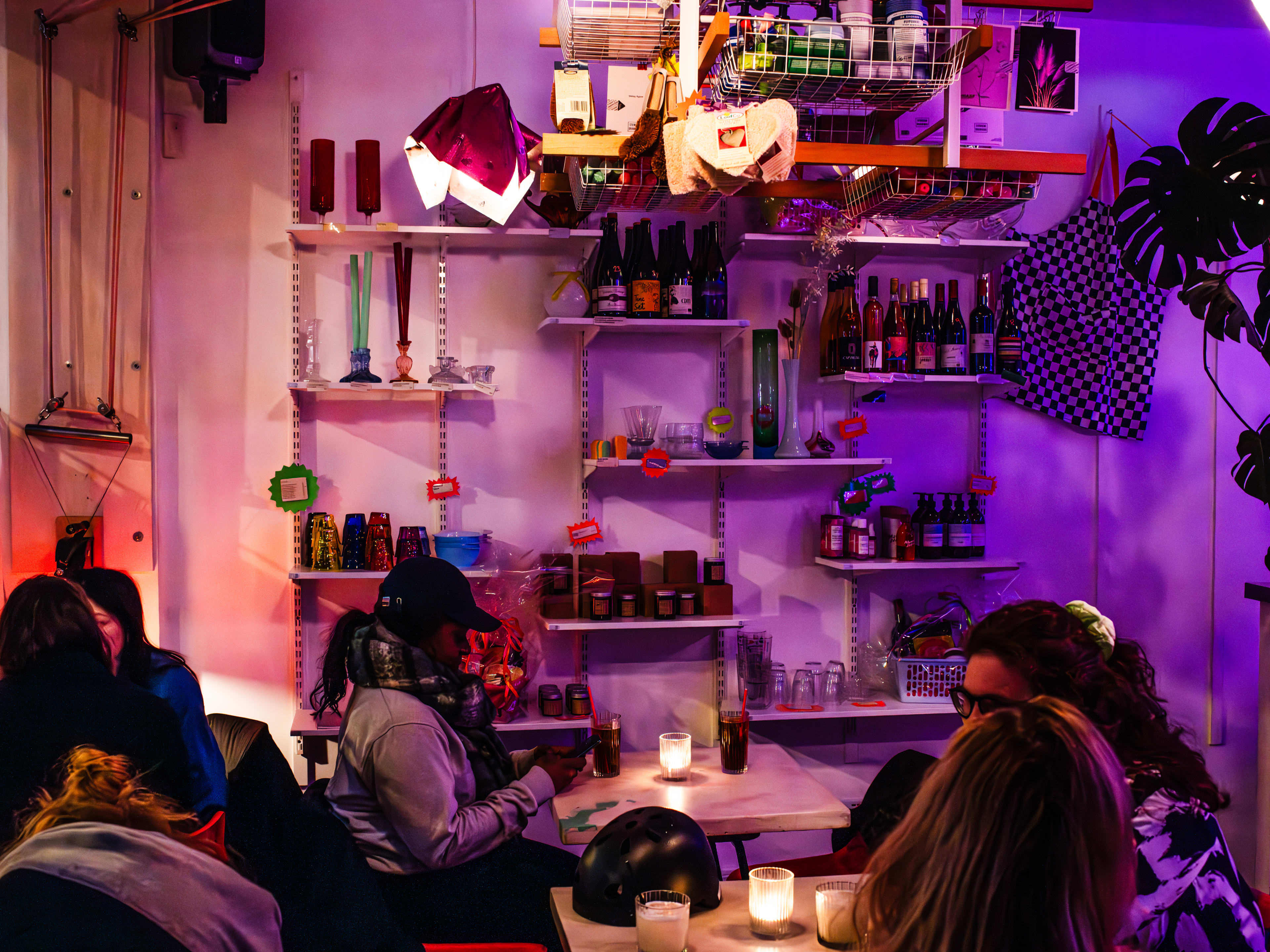 The interior of a small, dimly lit and purple-tinged cafe/bar at night with several groups of people at tables.