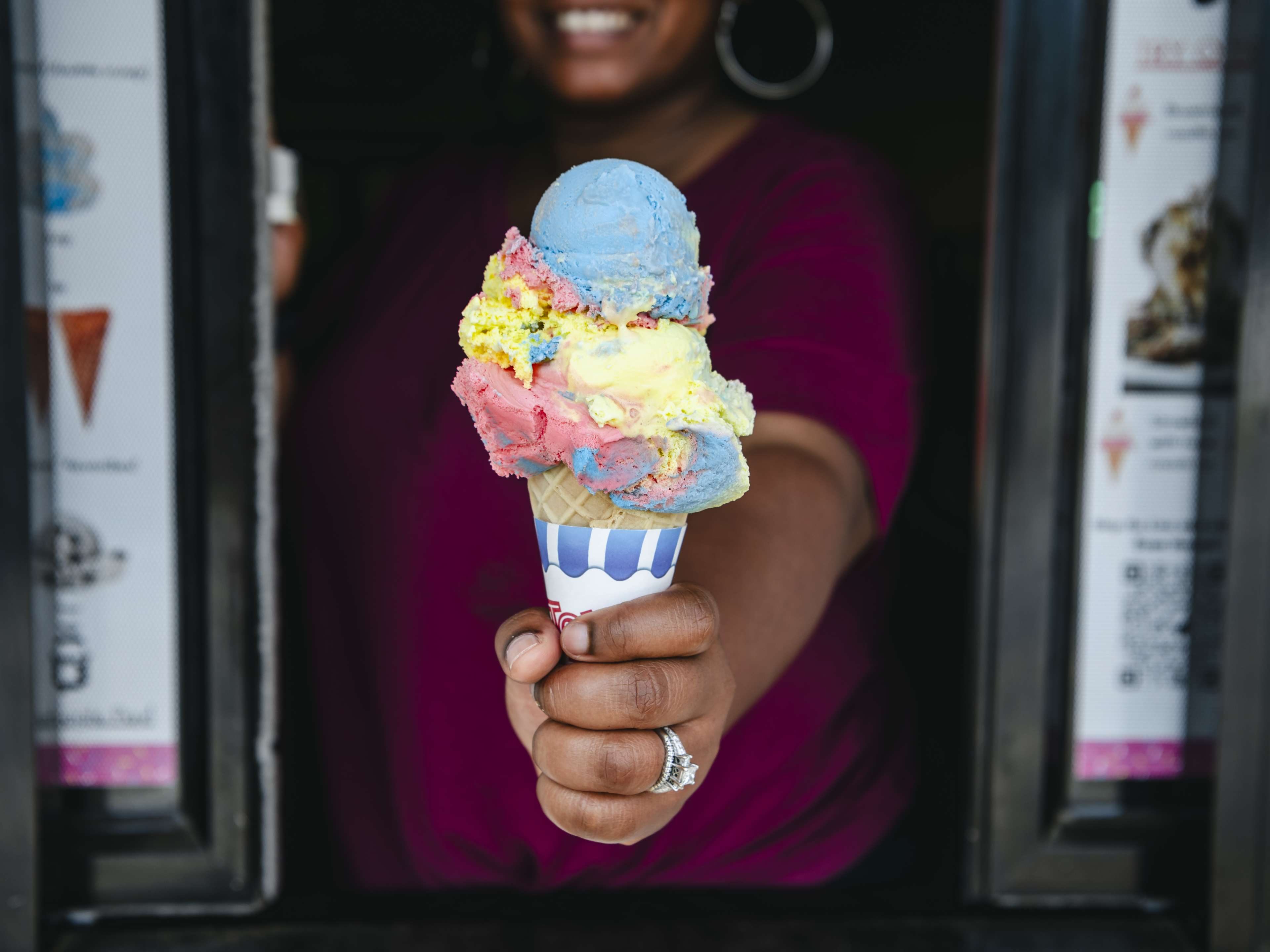 Woman holding rainbow colored ice cream in a cone.