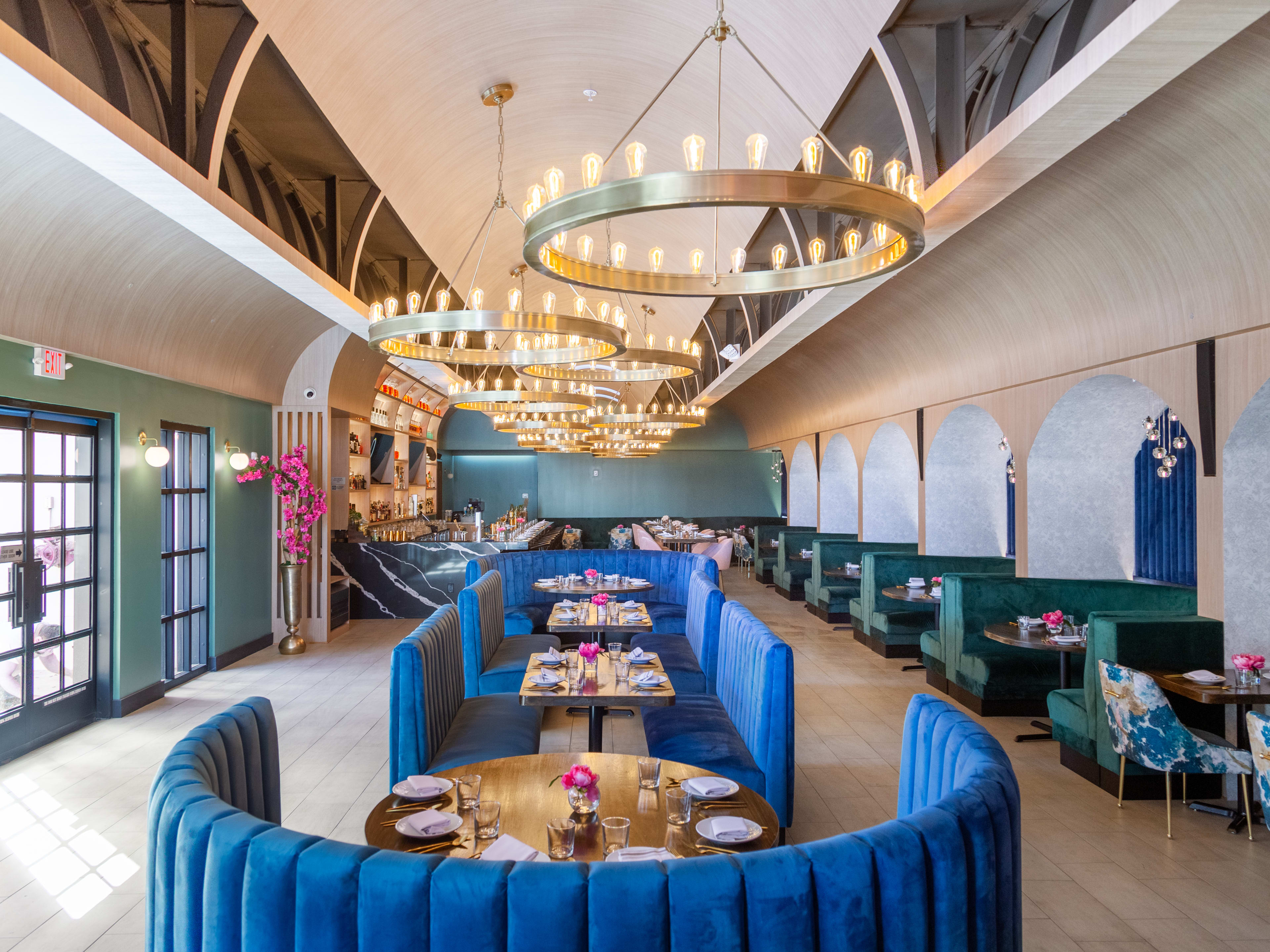 vaulted ceiling long narrow restaurant with bright blue and emerald green booths and gold chandeliers