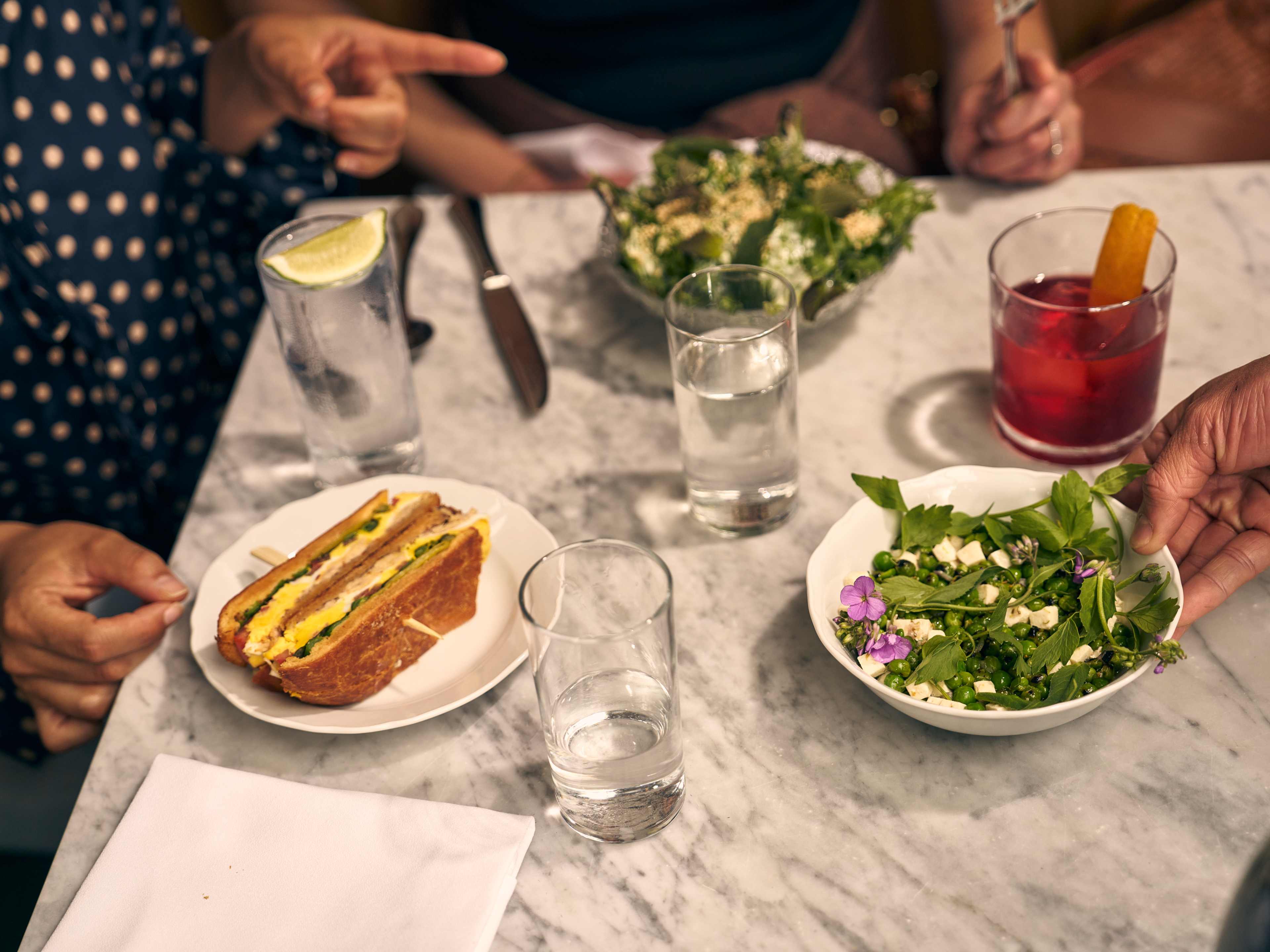 peas and sandwich on a table with people's hands reaching for food at Cafe Mado