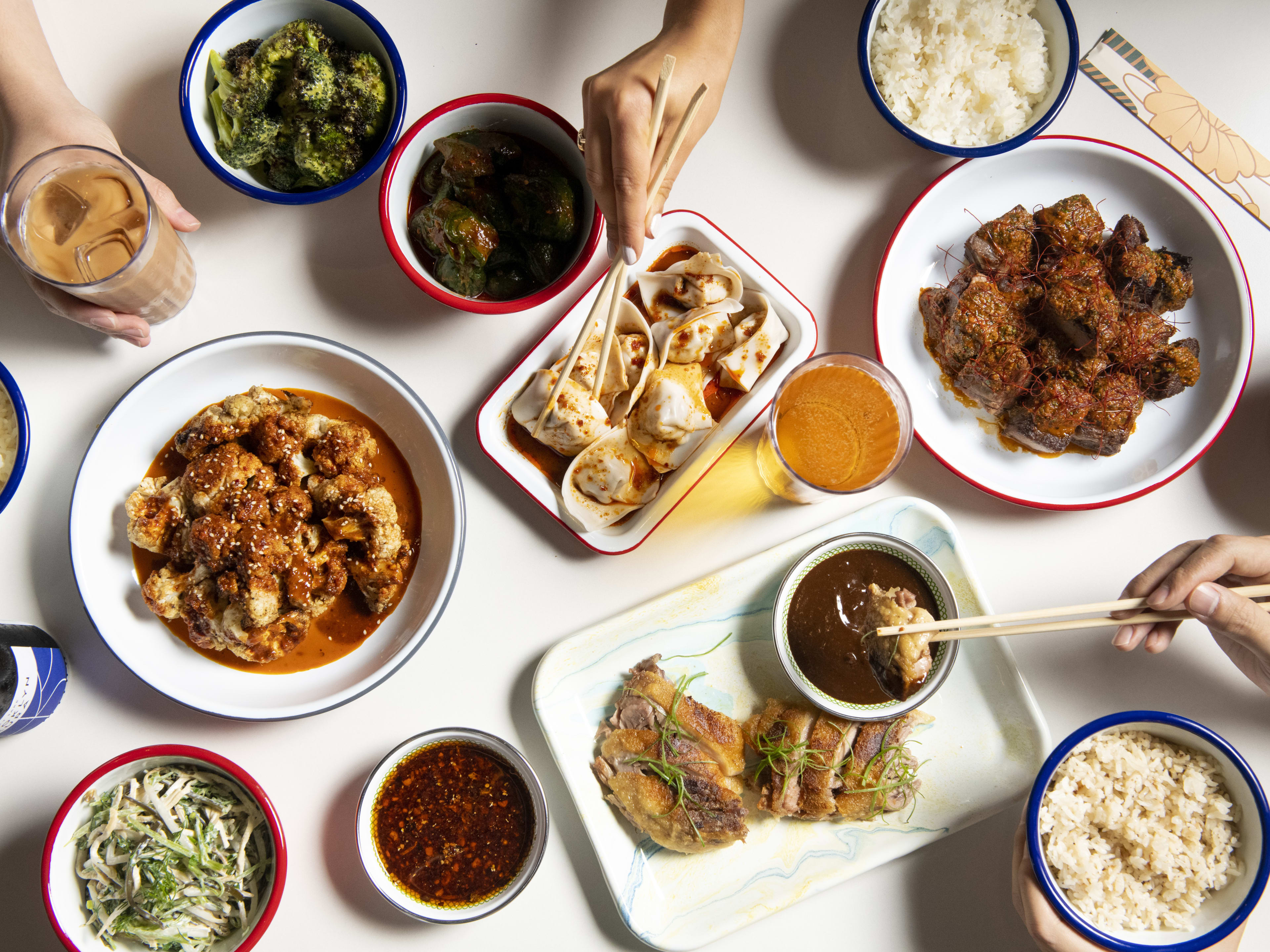 Milu spread of Chinese food with hands reaching in to grab dumplings with chopsticks