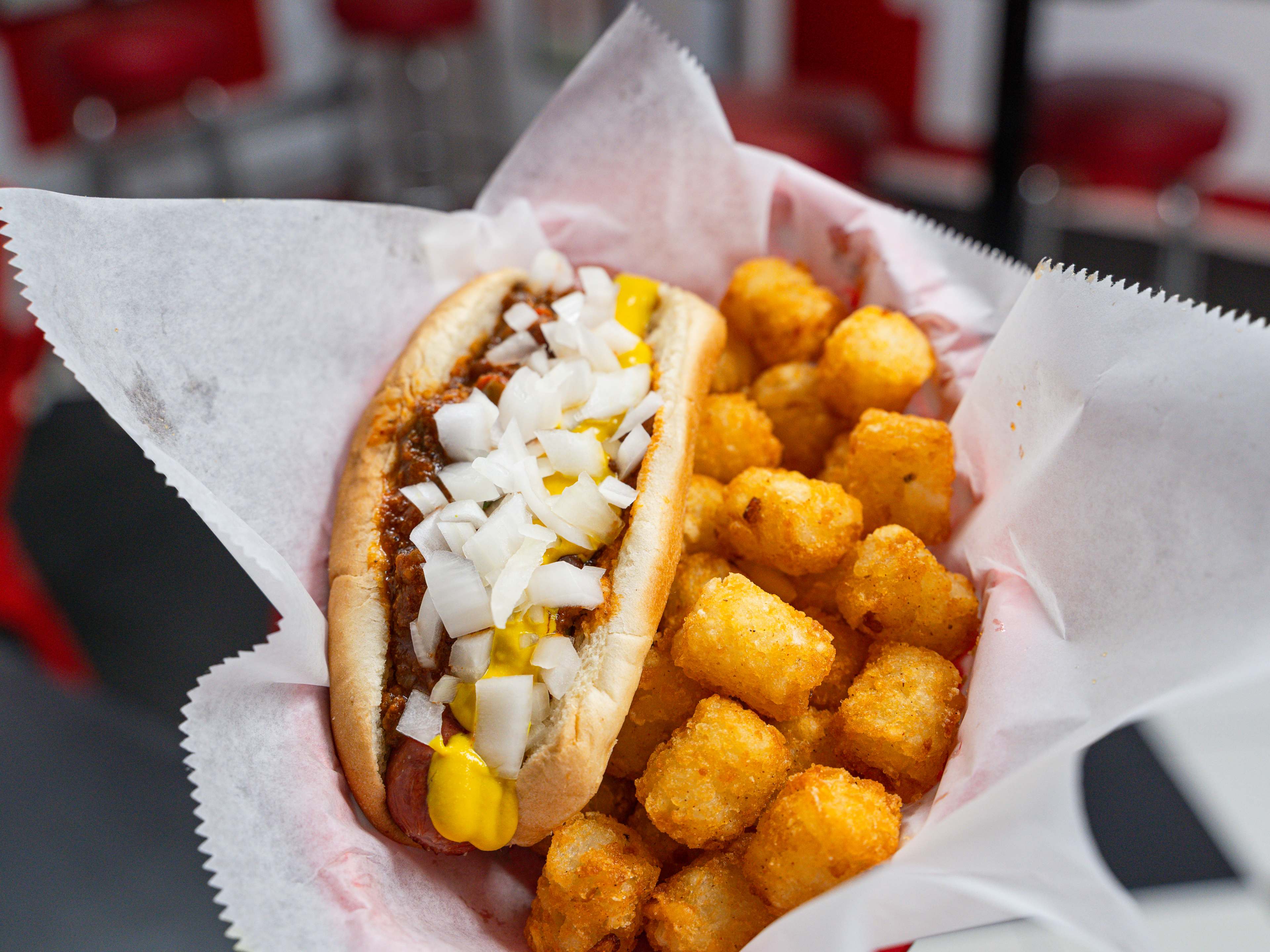 Chili dog topped with onions and a side of tater tots in basket