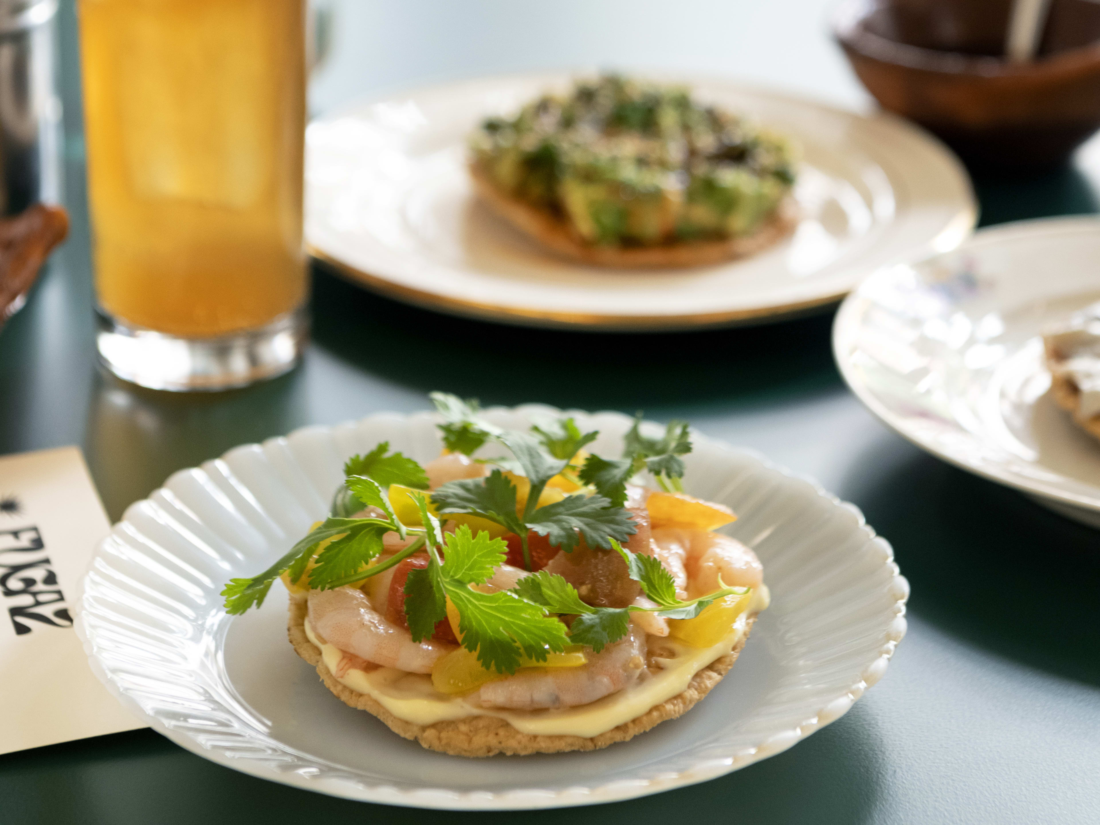 Variety of small tostada dishes with iced cocktail on green table at Fugaz