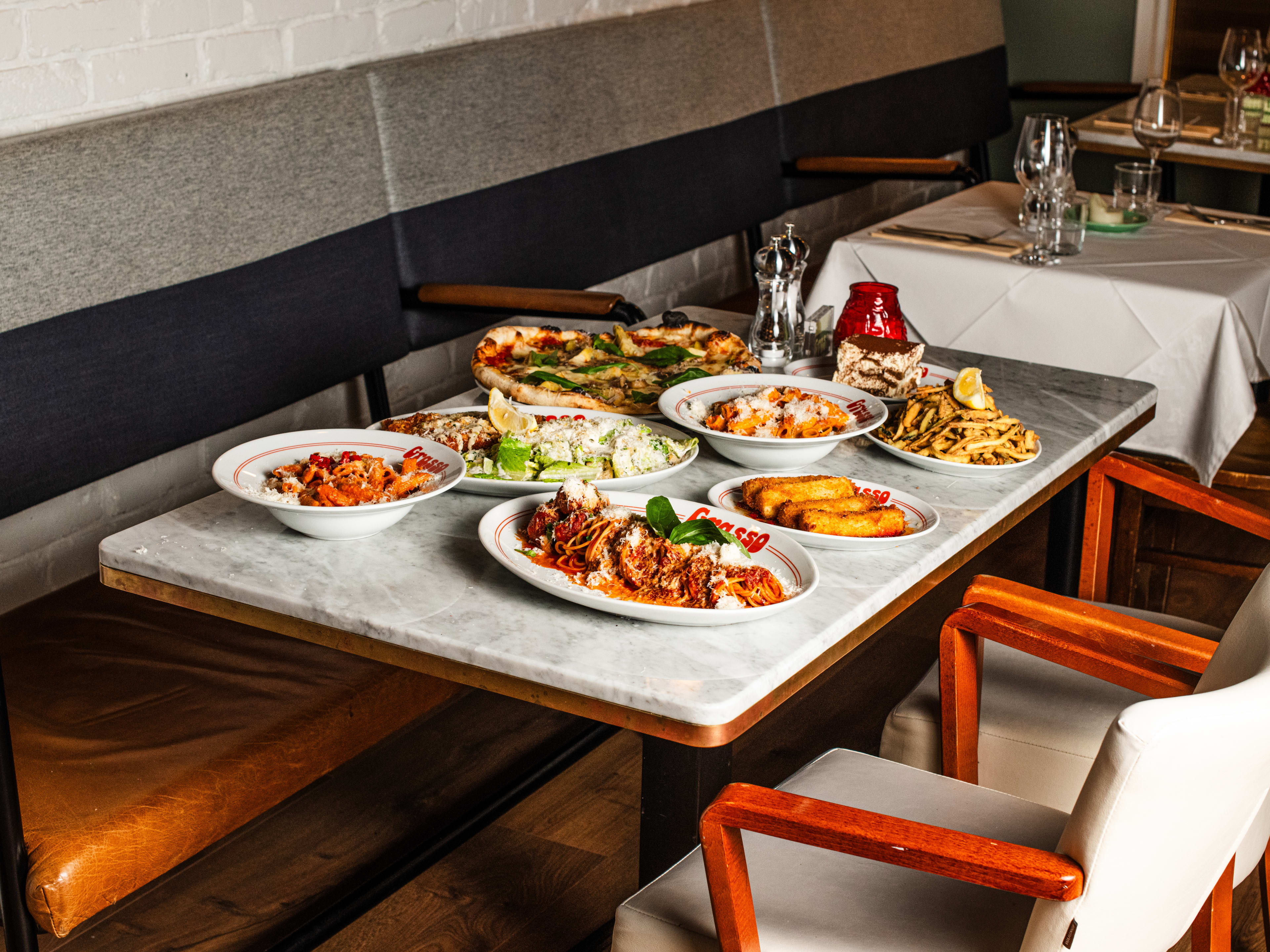 Italian dishes like pasta and pizza on a marble-look table.