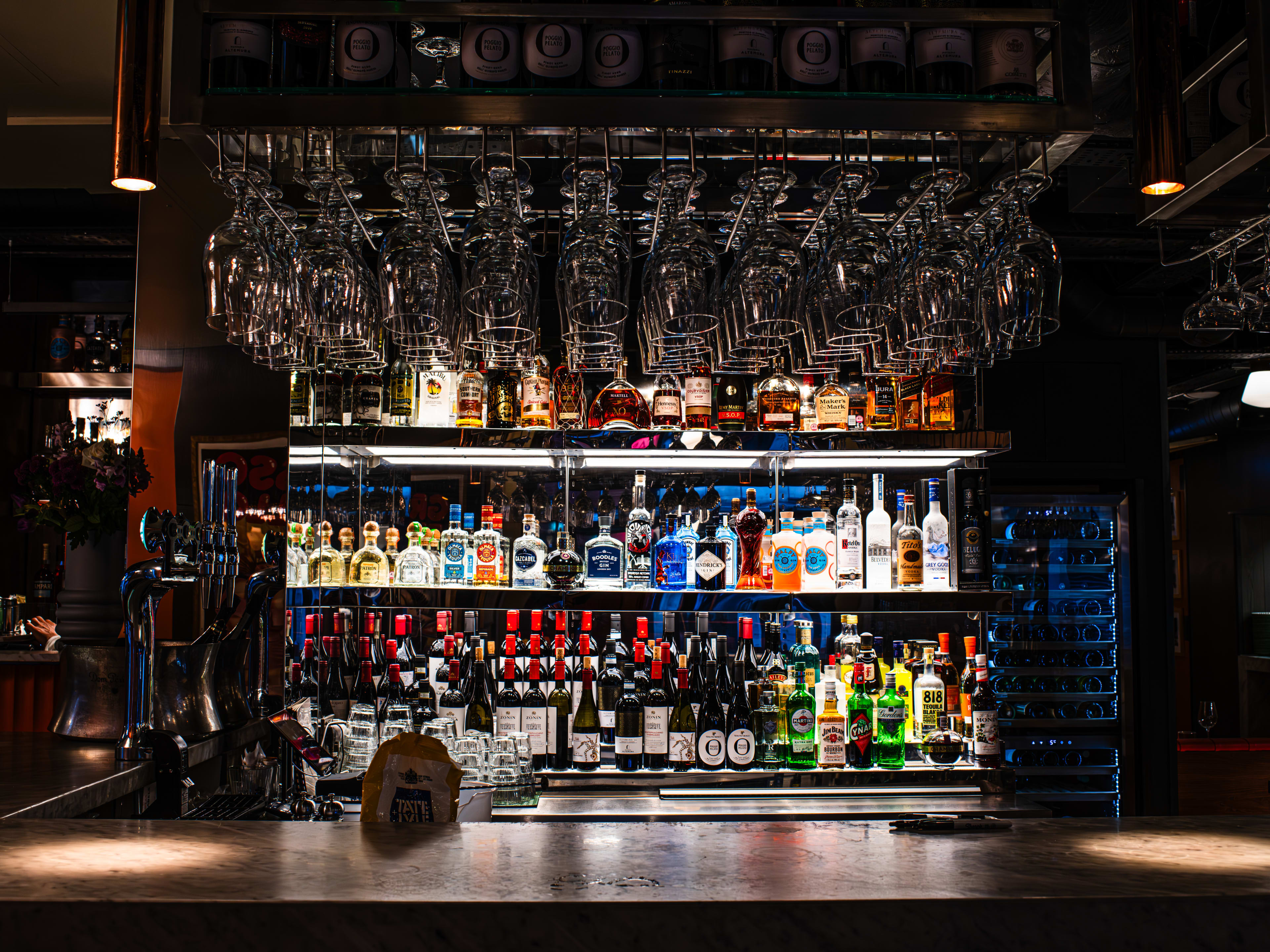 A bar stocked with bottles of wines and spirits, and hanging wine glasses.