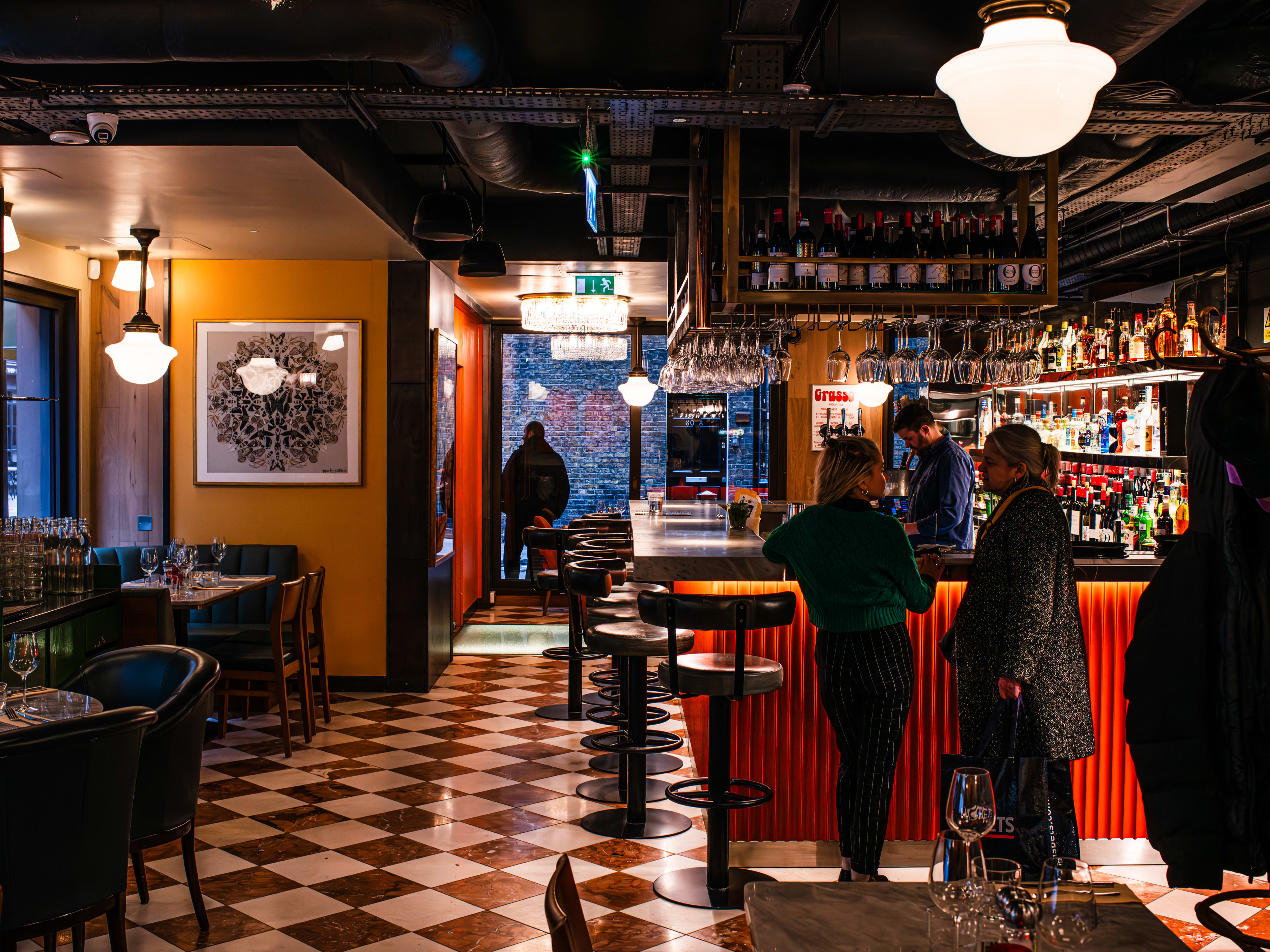 Interior of a restaurant with checkered floor tiling and bottles around a bar.