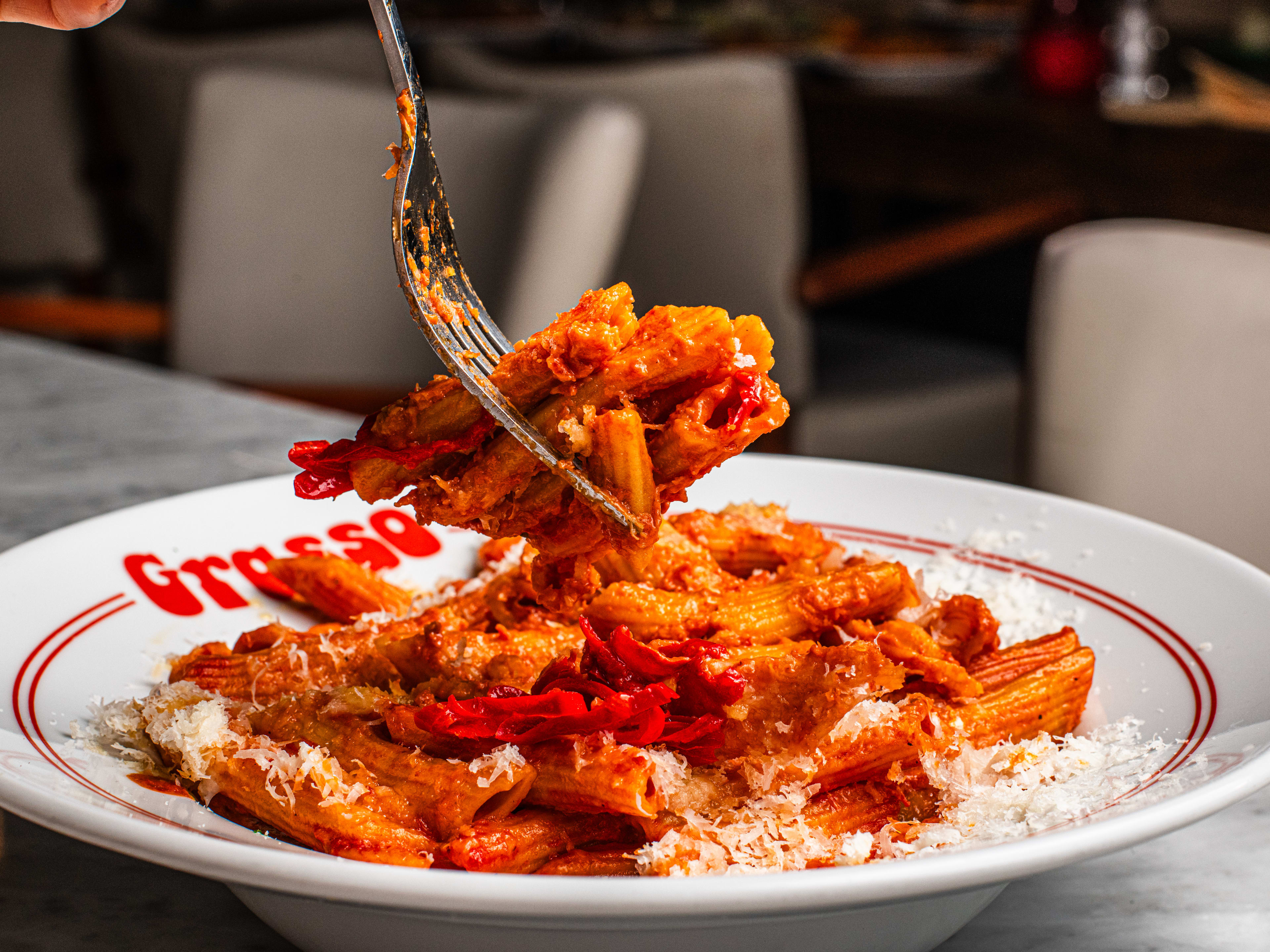 A plate of penne alla vodka with a fork lifting up several pieces of pasta.