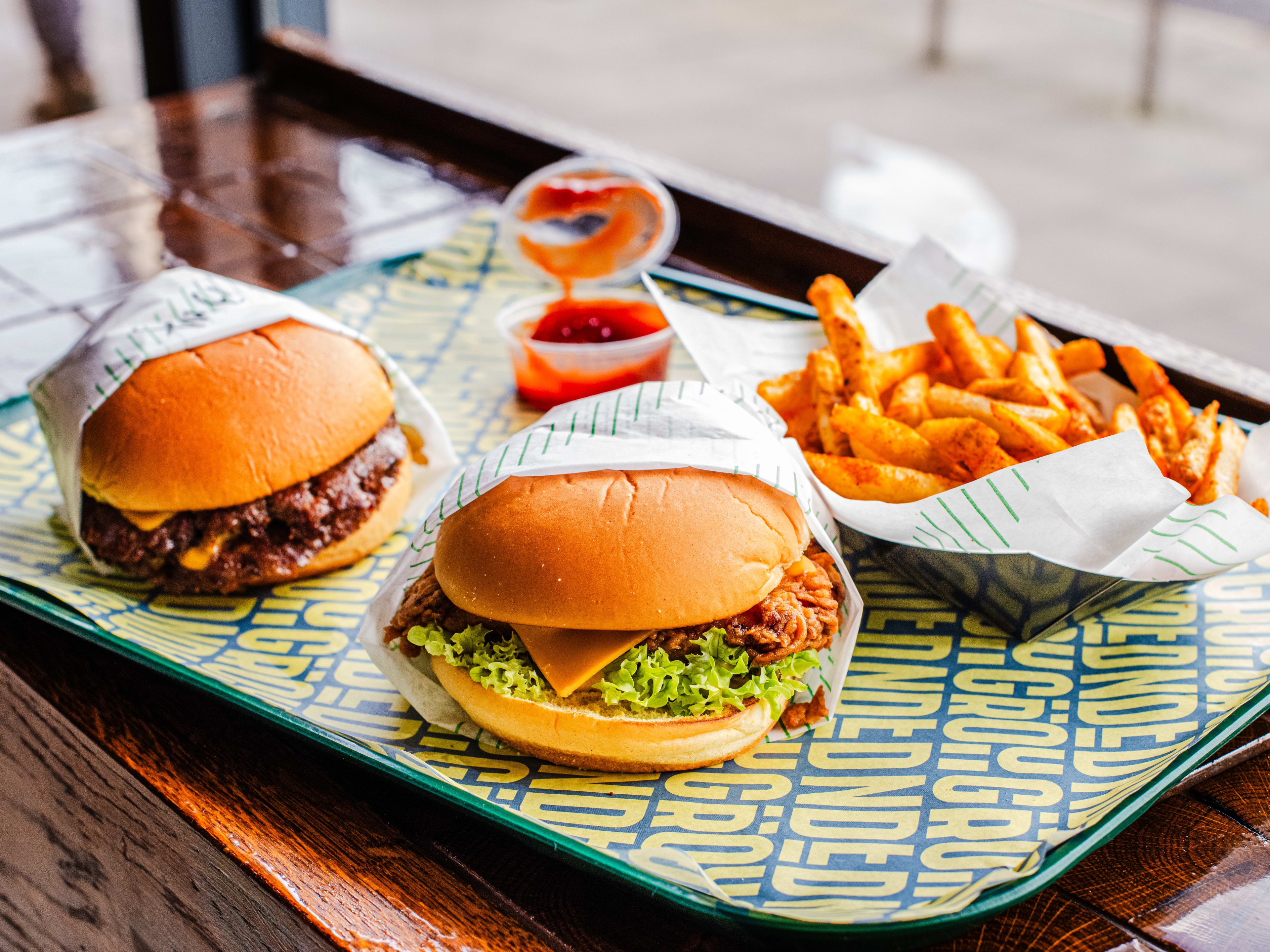 Two burgers and fries on a tray lined with Grounded Burger-logo paper.