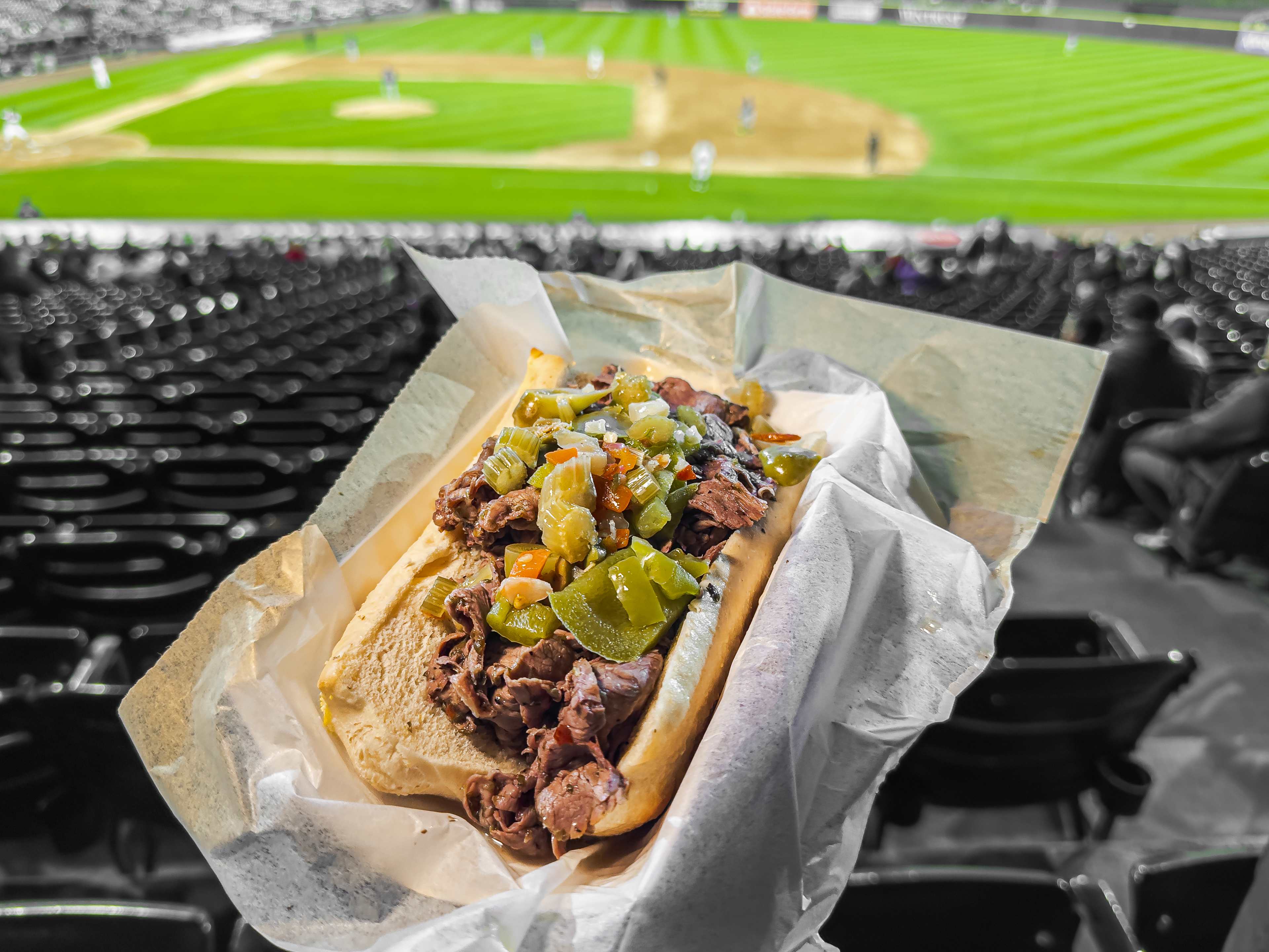 Italian beef held up in front of a baseball diamond and stadium seating