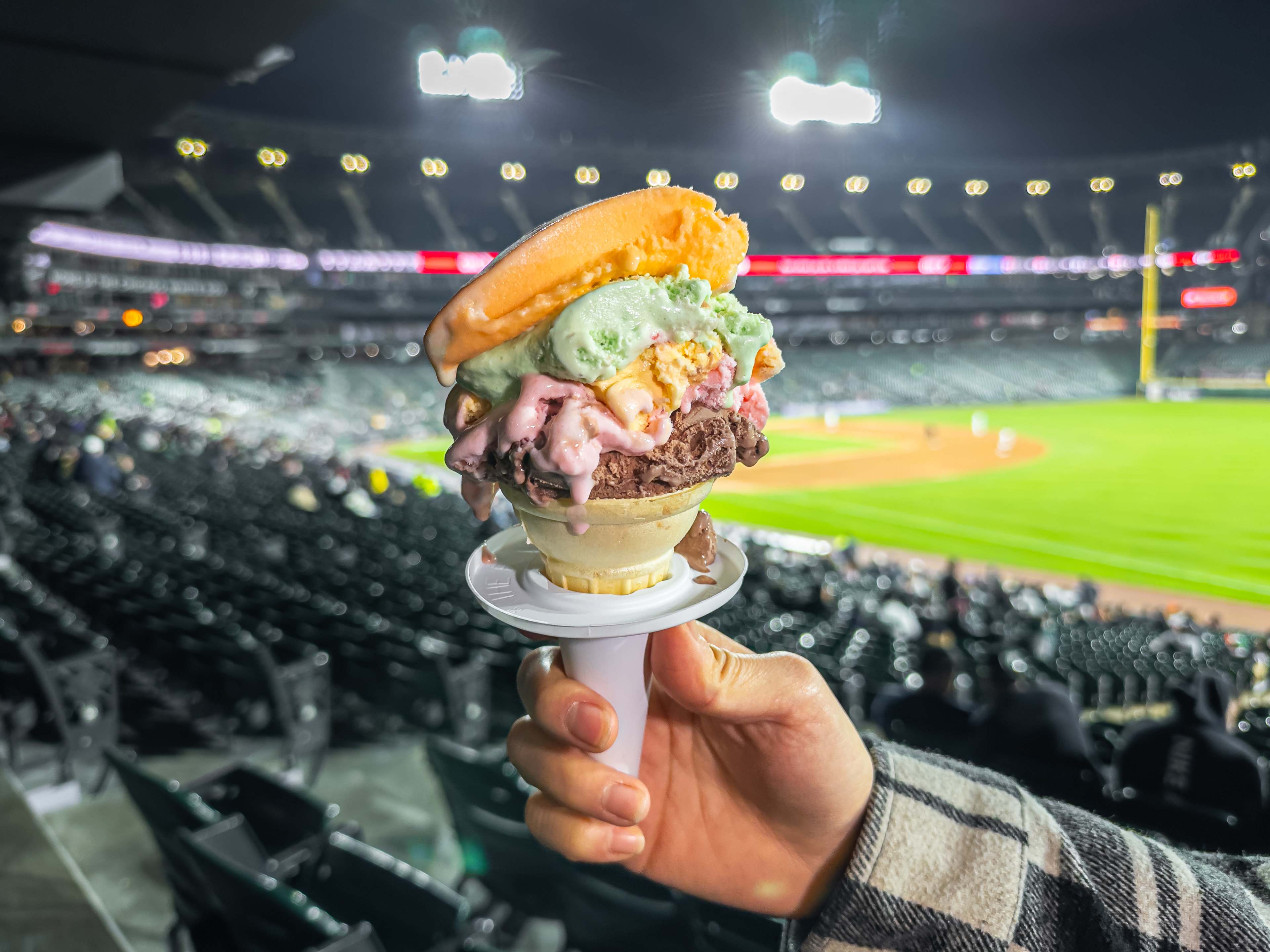 Rainbow cone held up in front of a baseball diamond and stadium seating