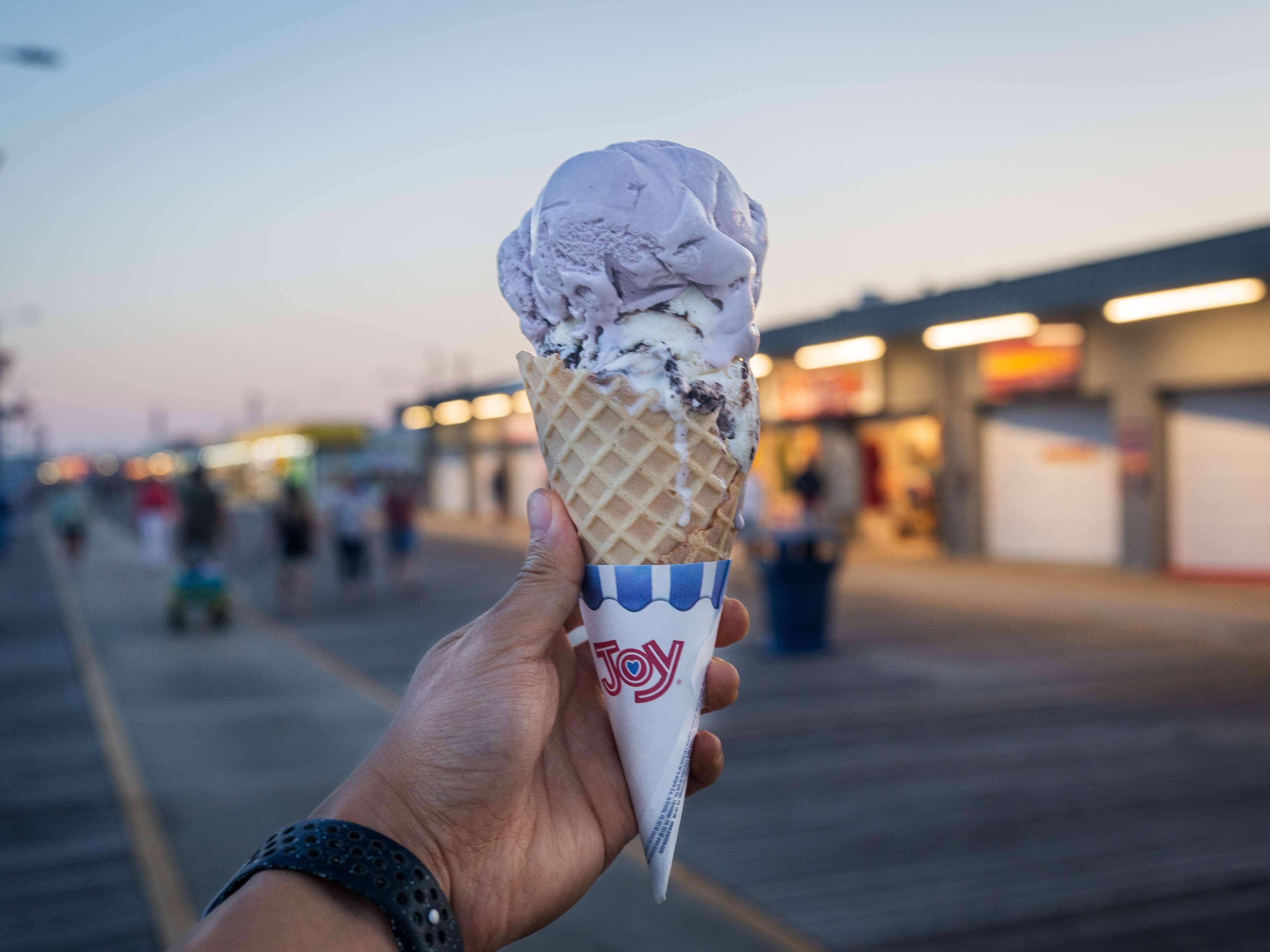 Hand holding waffle cone with a scoop of black raspberry and cookies n cream.