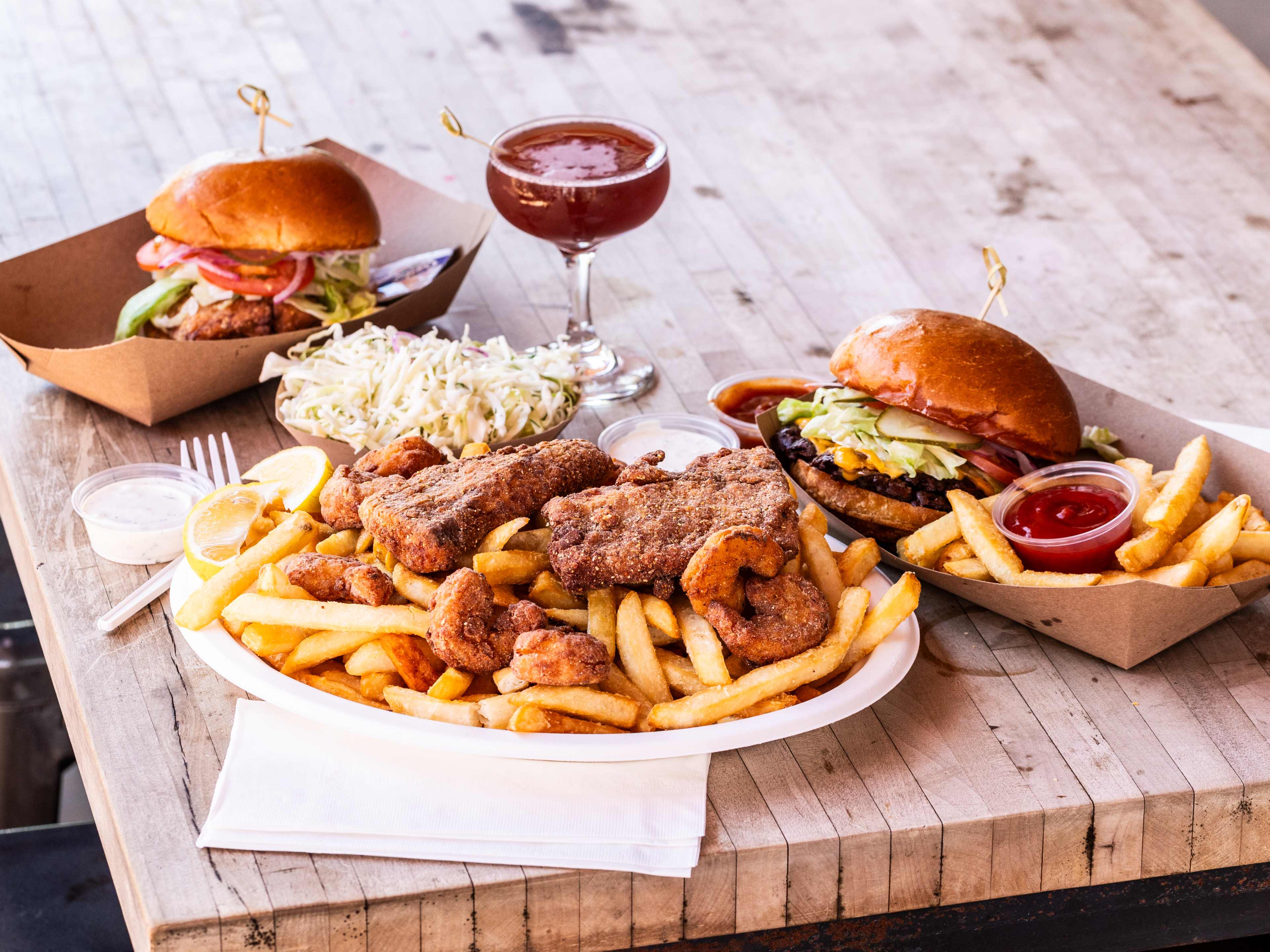 A spread of dishes and a cocktail from Huckleberry on a wooden picnic table.