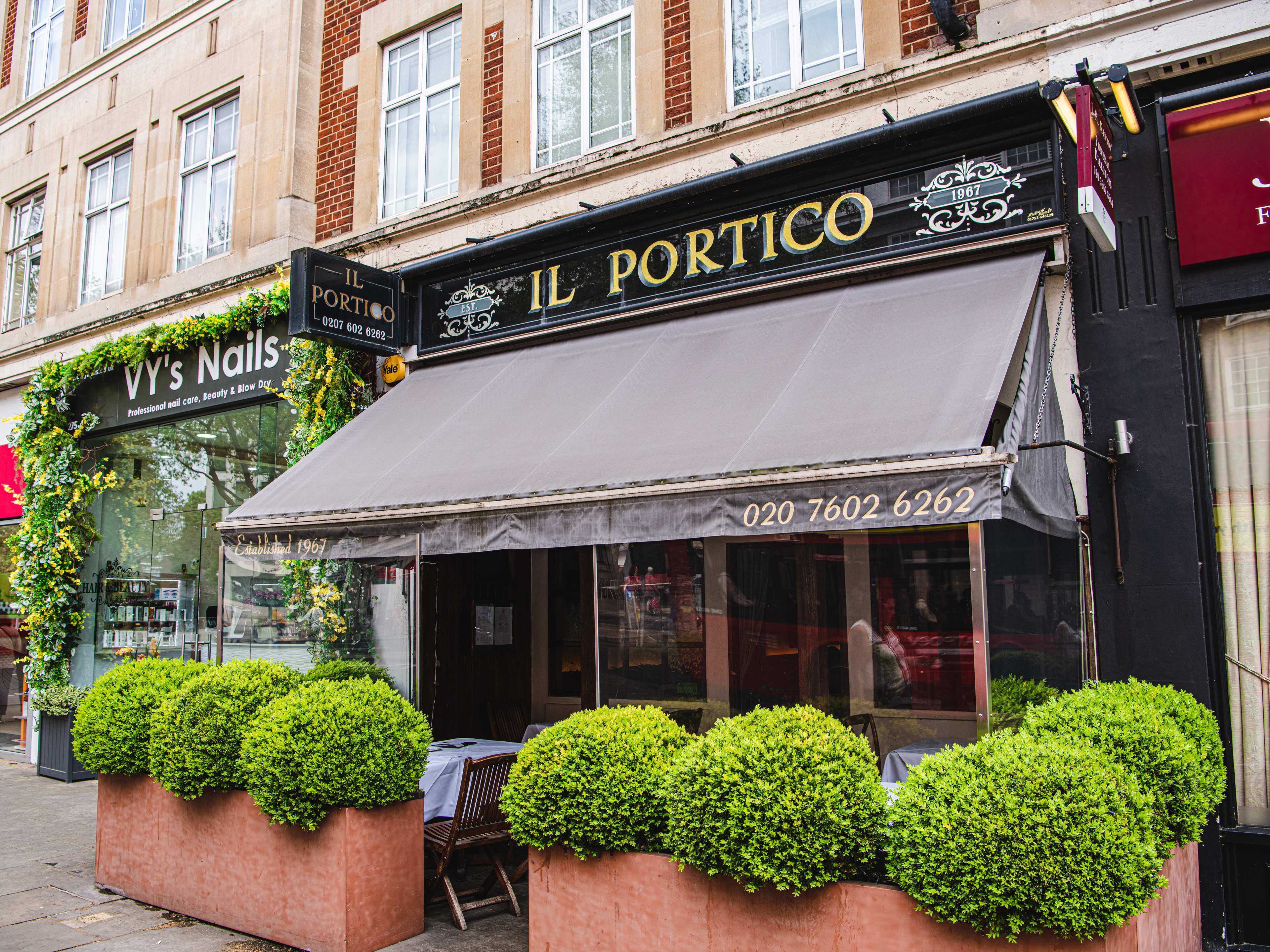 The exterior of Il Portico. There are hedges surrounded a few outdoor tables.