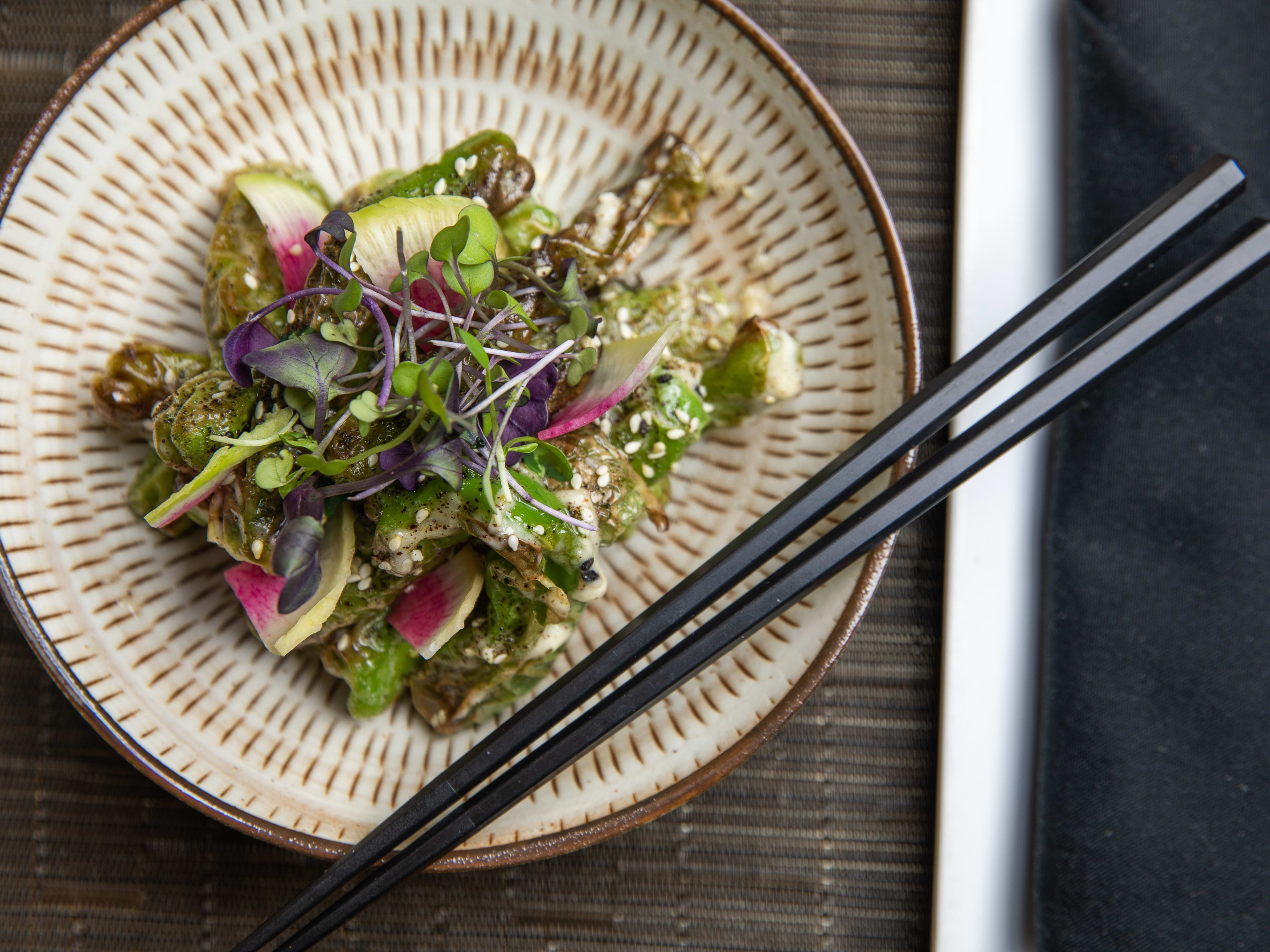 Plate of shishito peppers topped with watermelon radishes at O-Ku