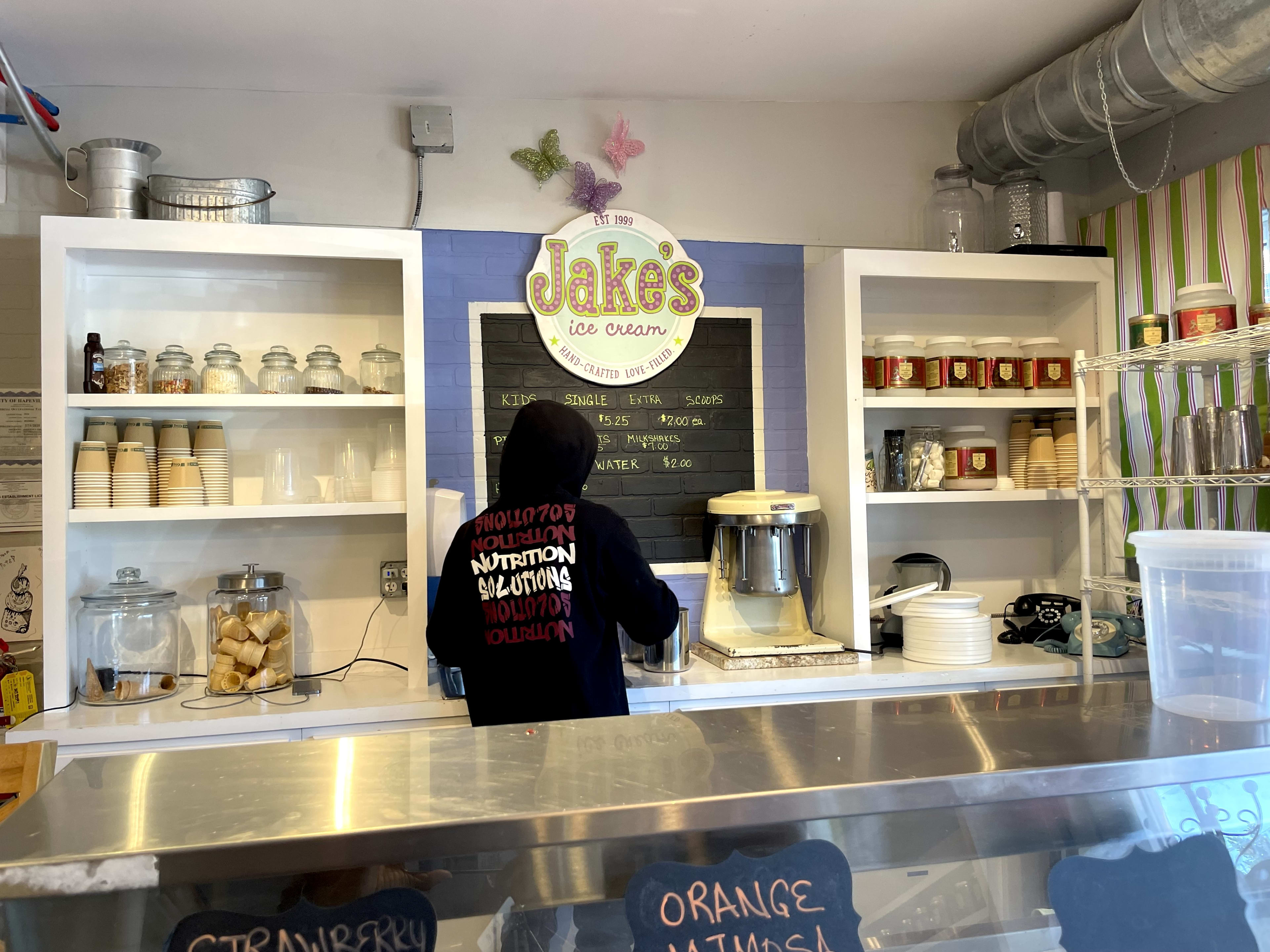 Jake's Ice Cream logo with white shelves and purple brick wall.