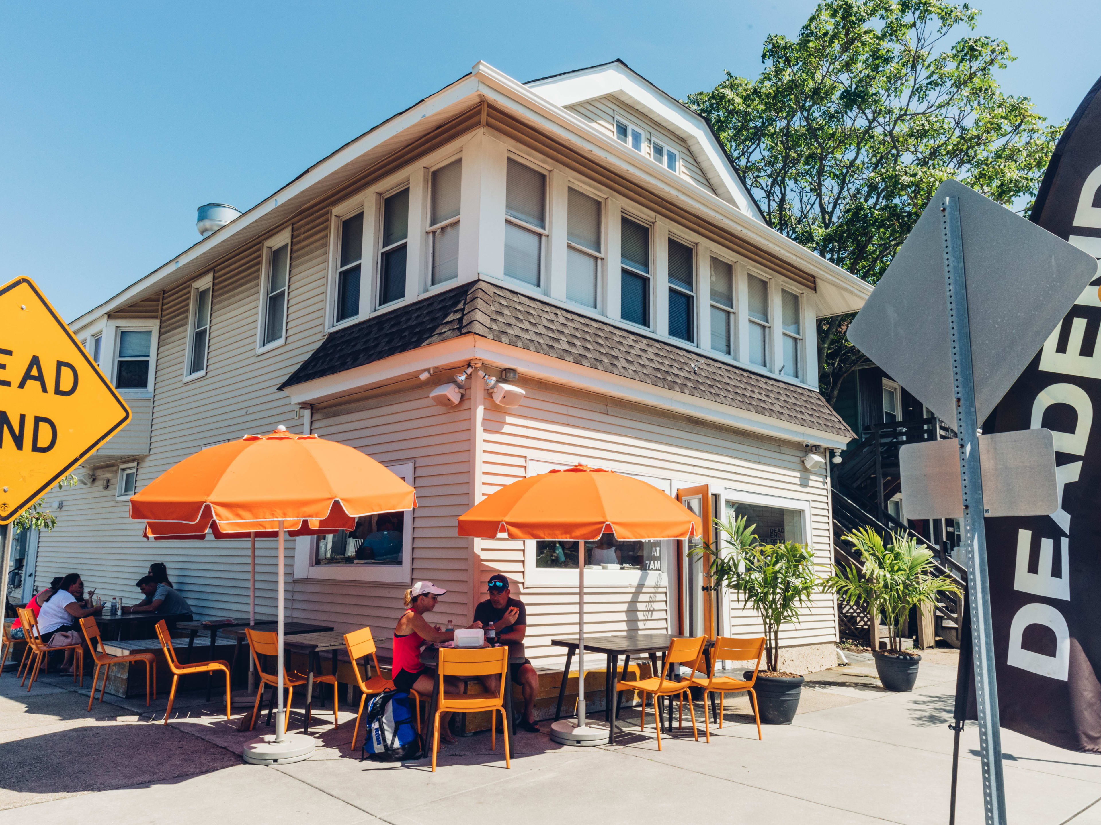 Dead End Bakehouse exterior with a dead end sign on the left and people seated at outdoor tables on the sidewalk