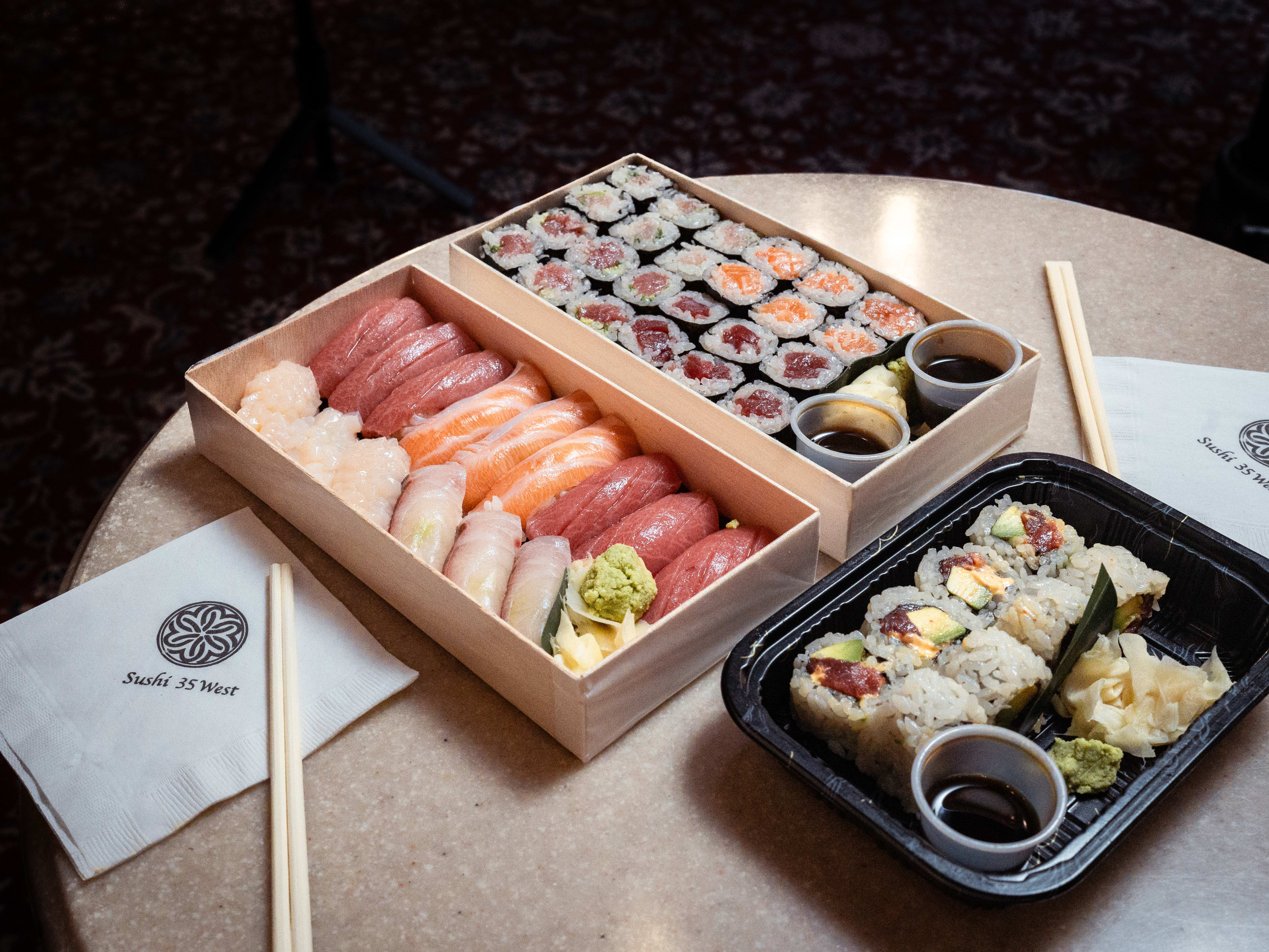 Sushi in a takeout container on a circular table with chopsticks and napkins from Sushi 35 West