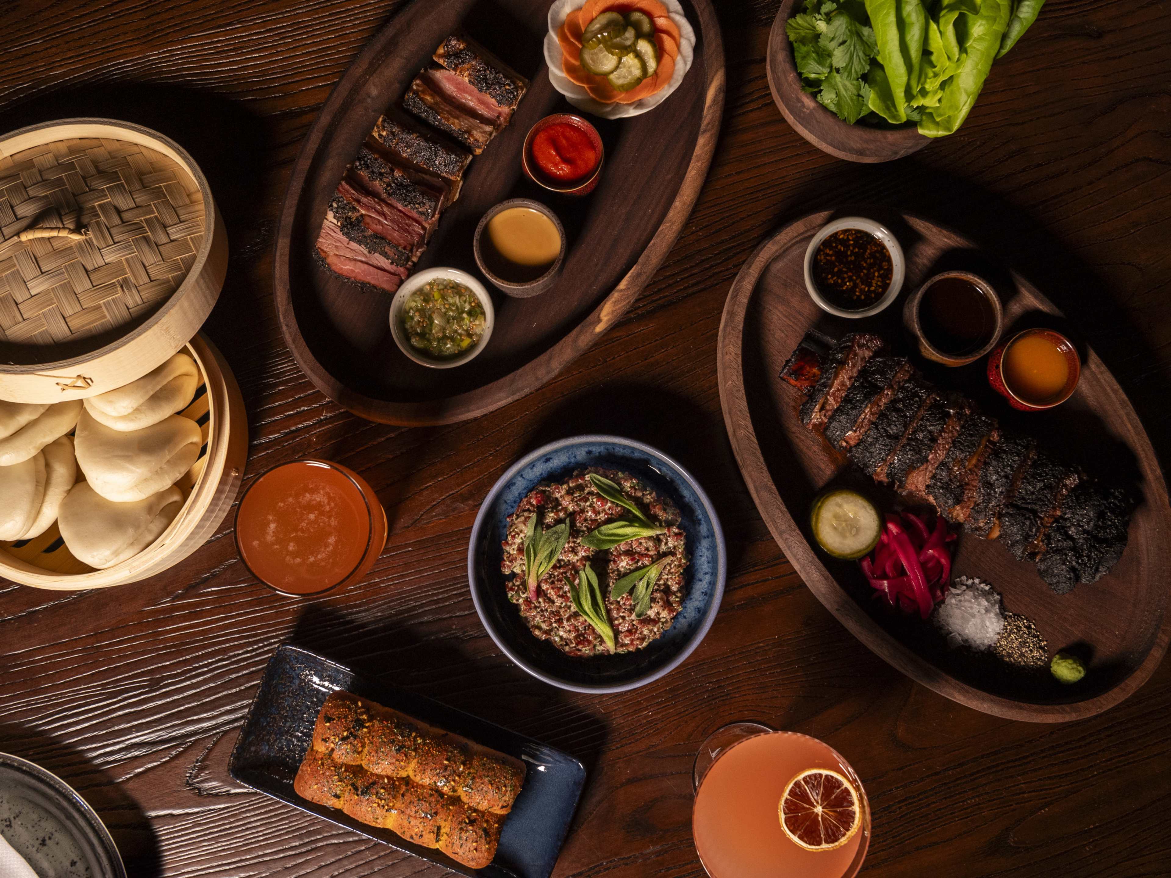 Spread of food and cocktails including bao buns, short rib, and pastrami