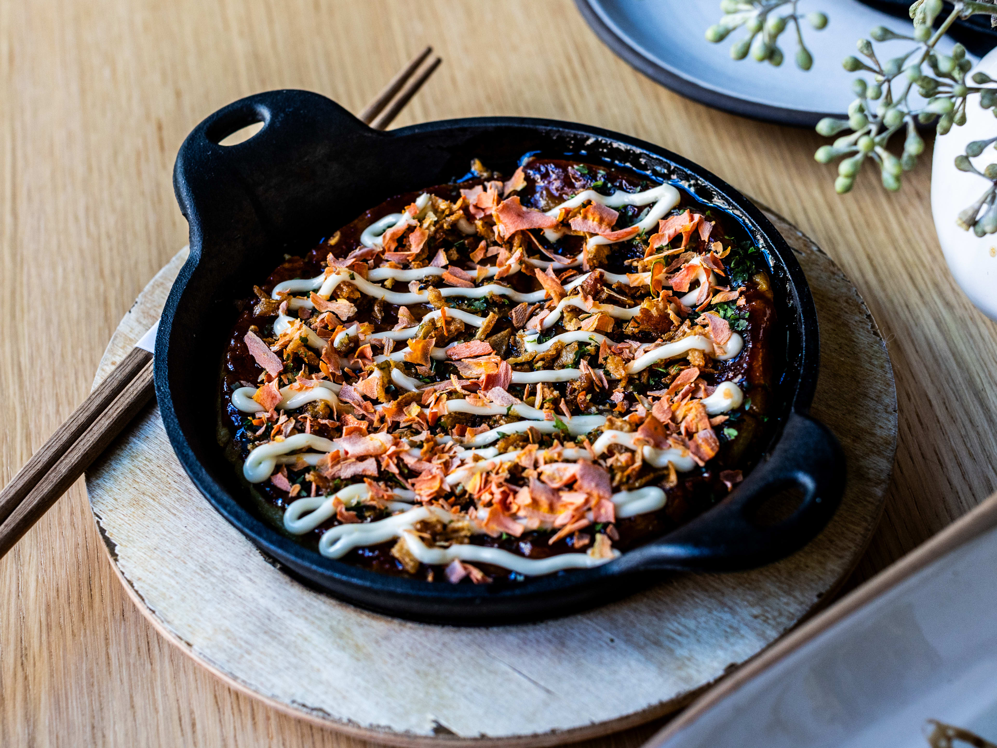 cast iron dish with a thin pancake topped with zig zags of dark sauce and white sauce topped with dried flecks of sweet potato