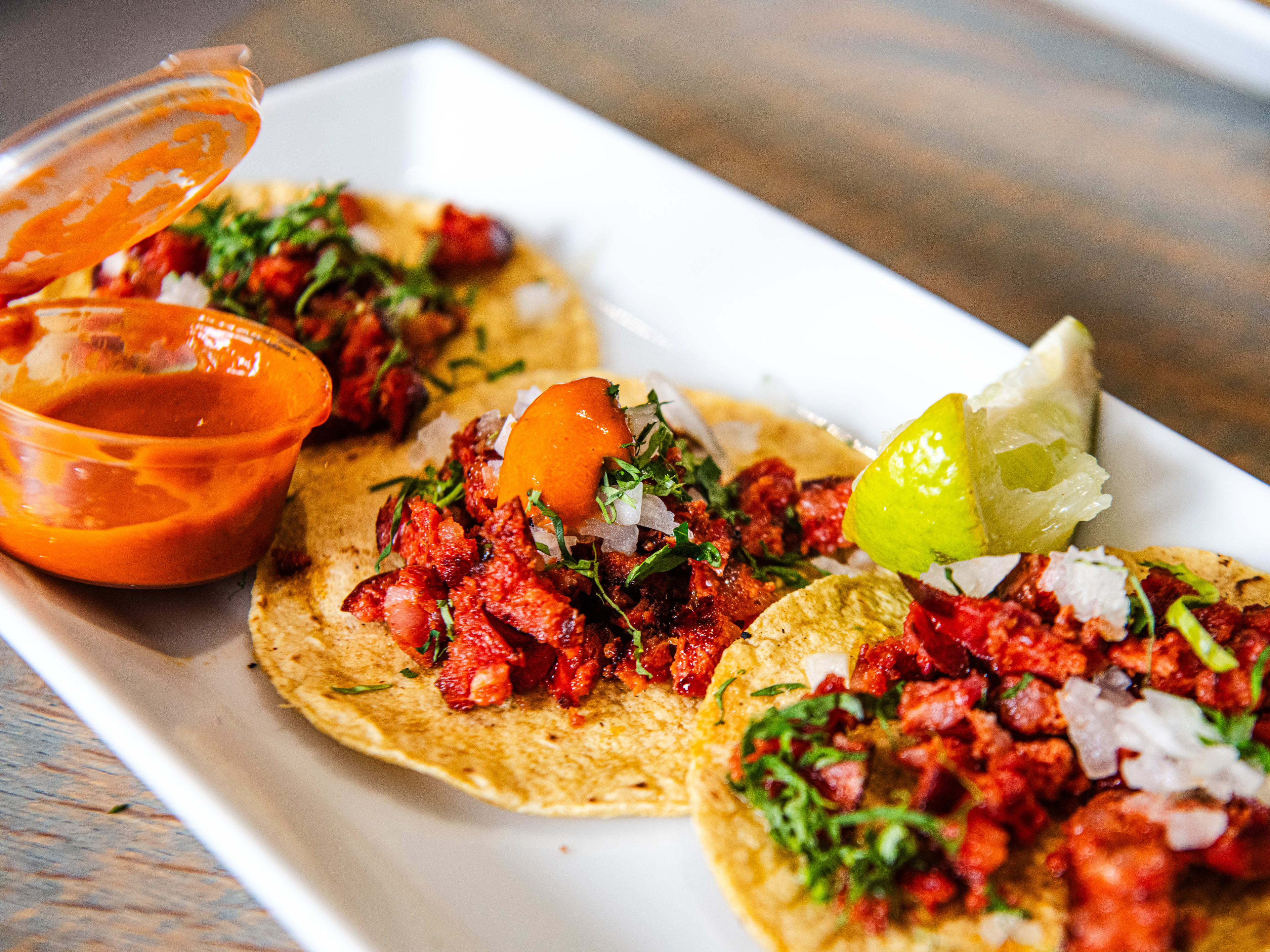 A plate of chorizo tacos from La Chingada with a pot of red salsa on the side.