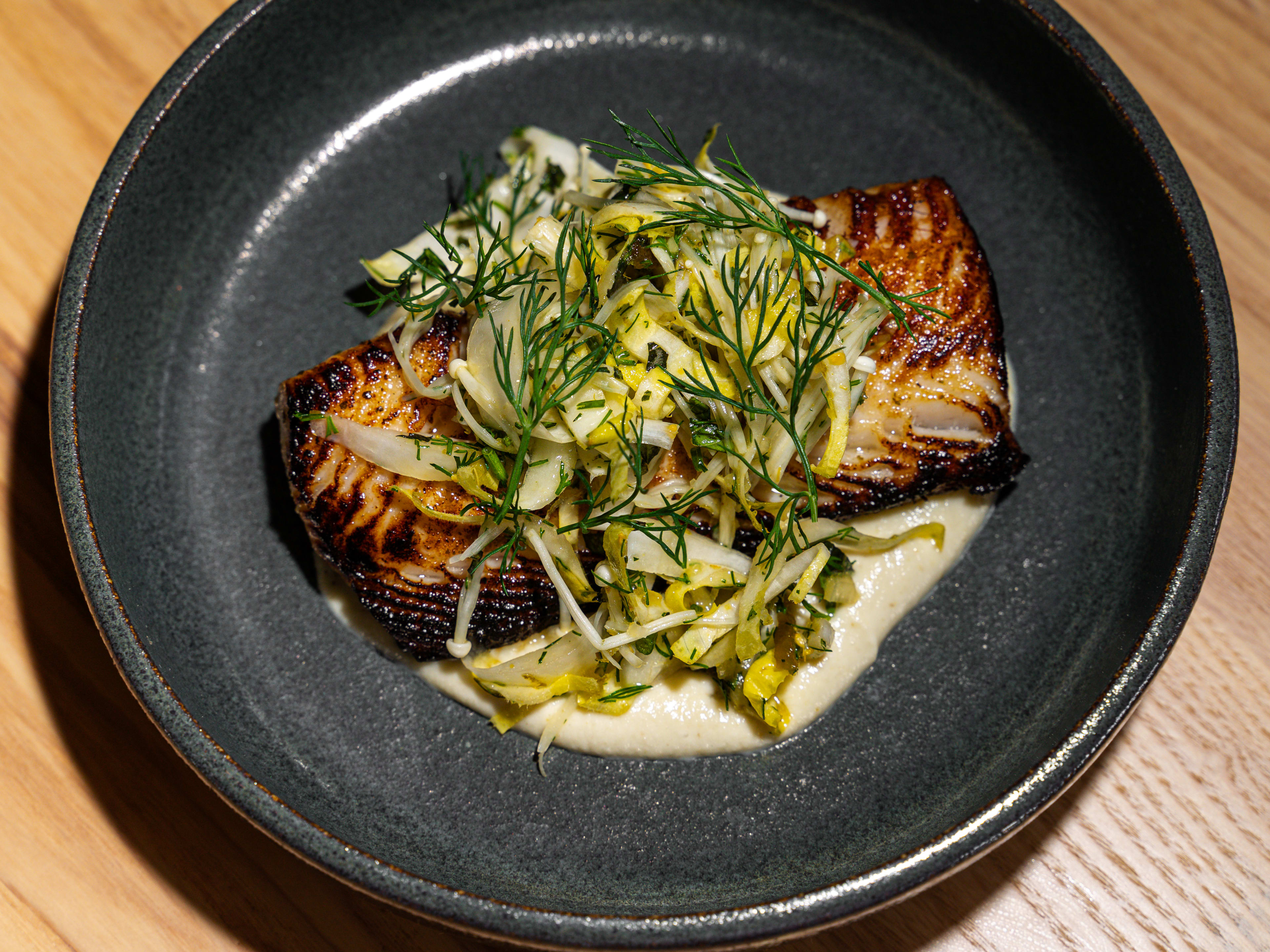 Piece of blackened cod sitting on a puree topped with mushrooms, endive and fennel