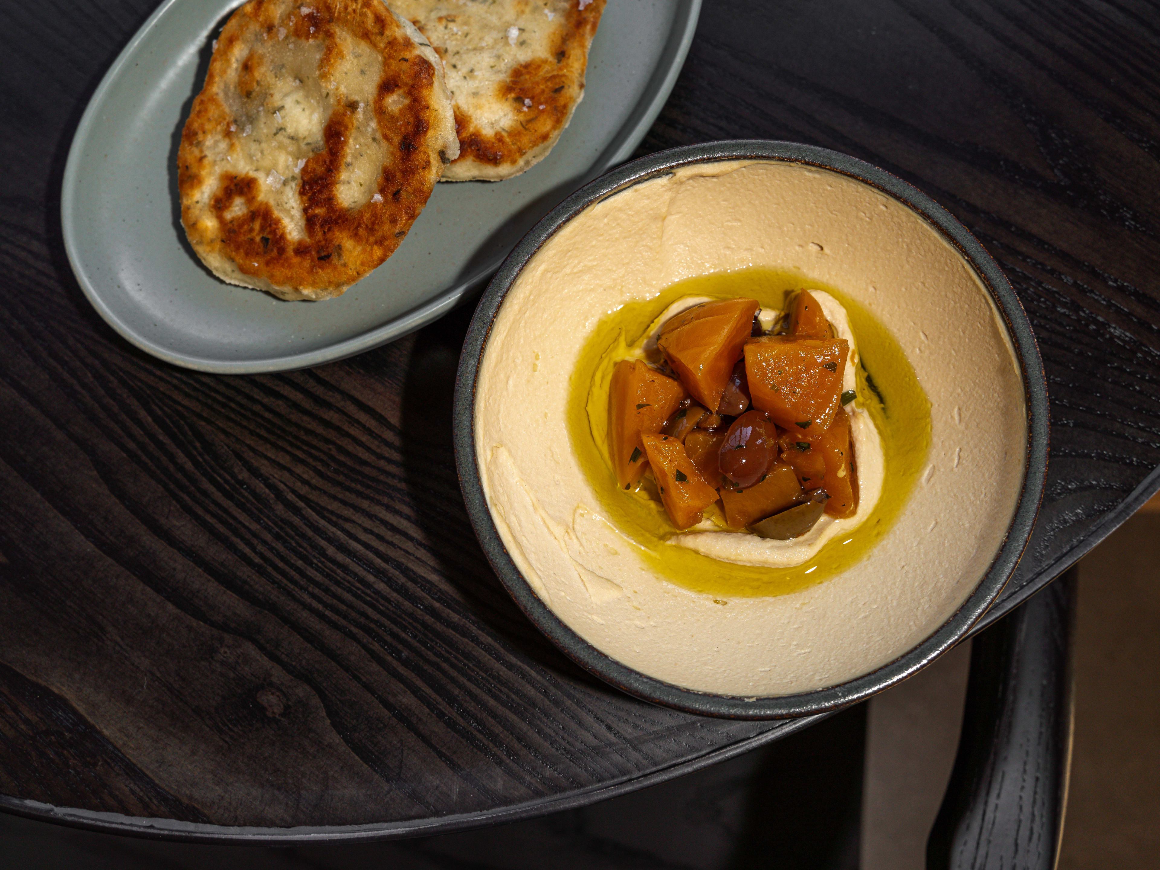 Table with a plate of griddle bread and a bowl of smooth hummus topped with beets