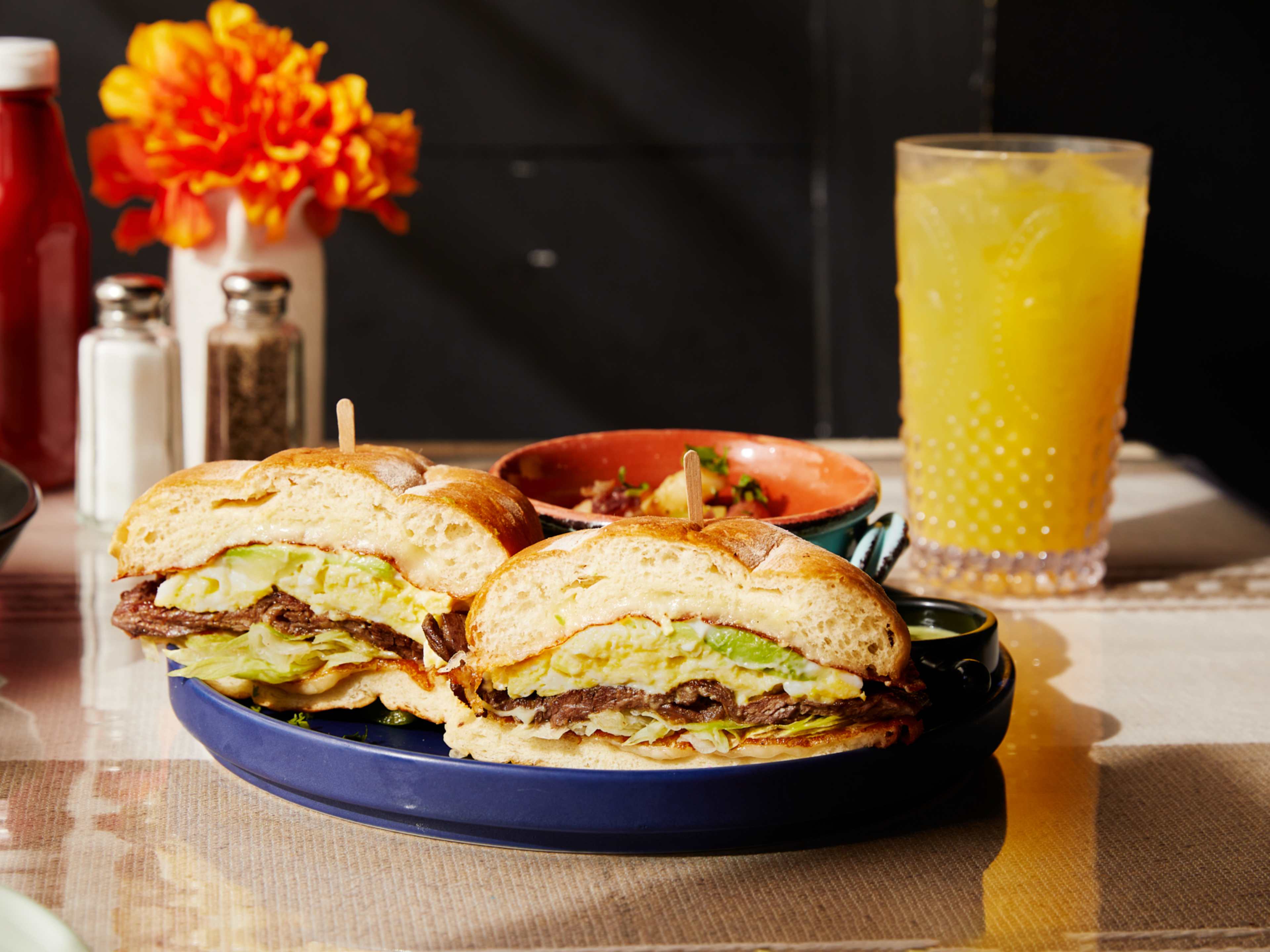 breakfast sandwich with avocado, egg, and meat, on a fluffy bun with juice in the background