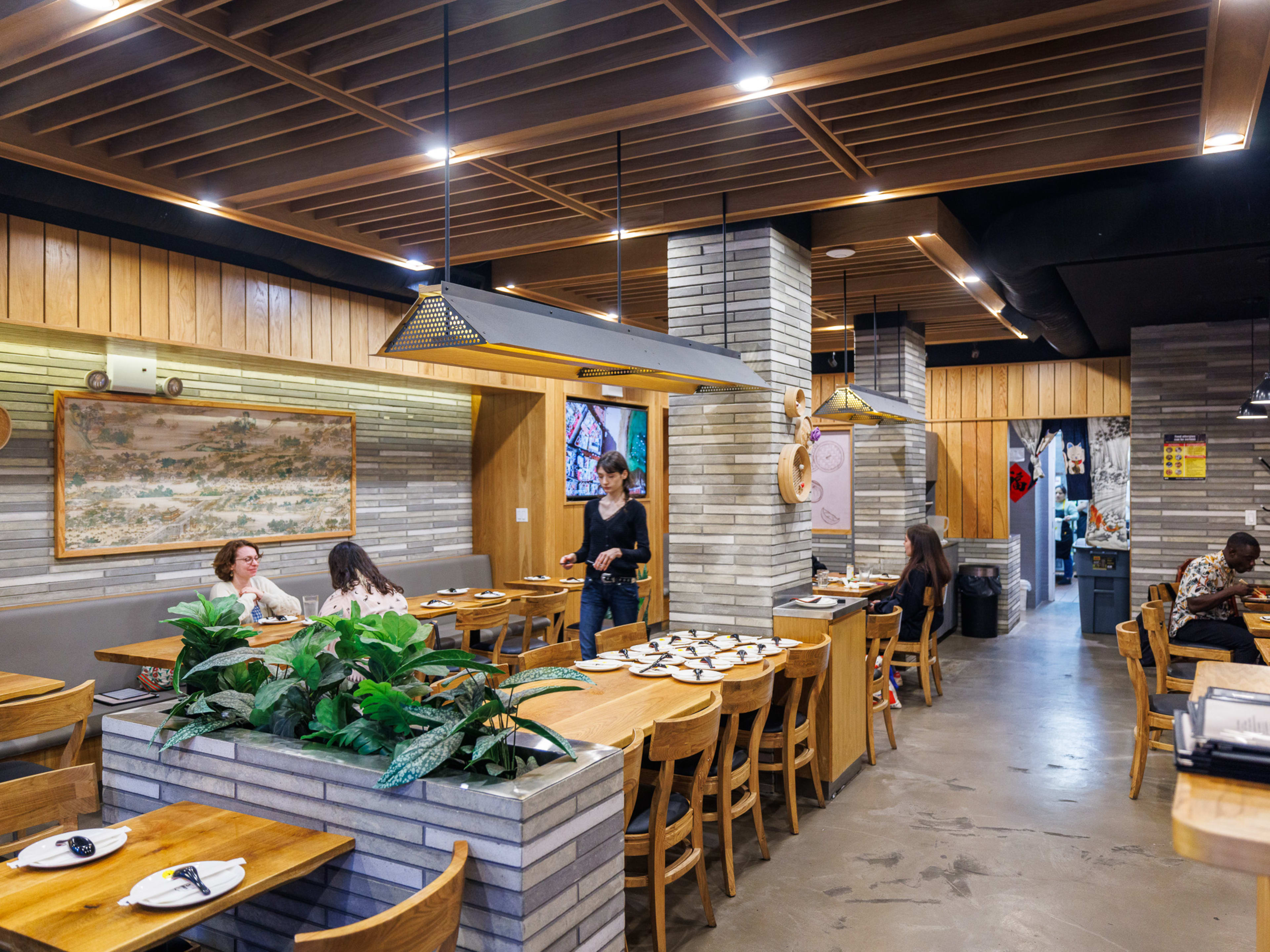 Three Times interiors with gray stone tile walls and people seated at wooden rectangular tables