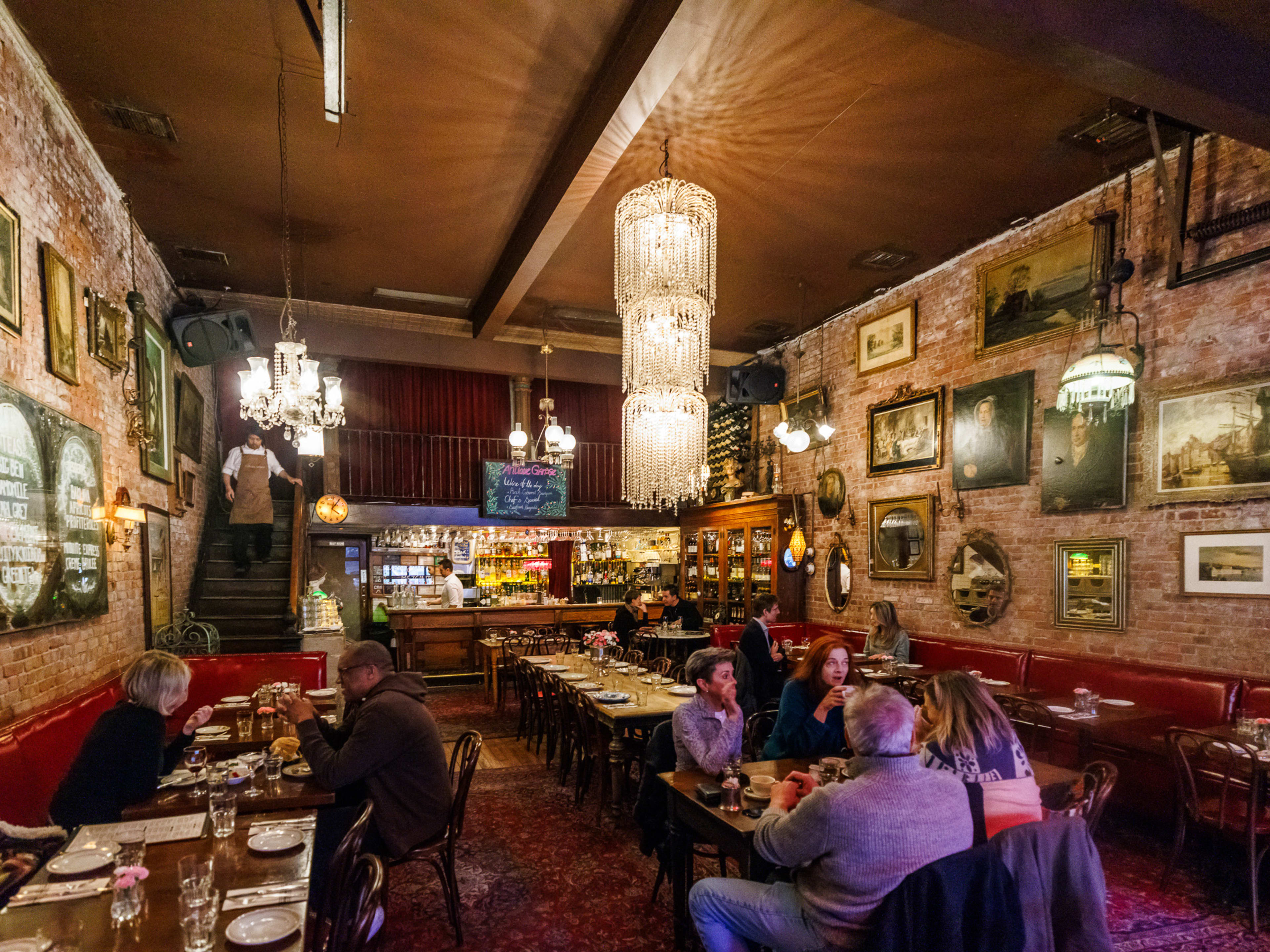 Antique Garage interior with brick walls, framed art, booth seating, and multiple chandeliers