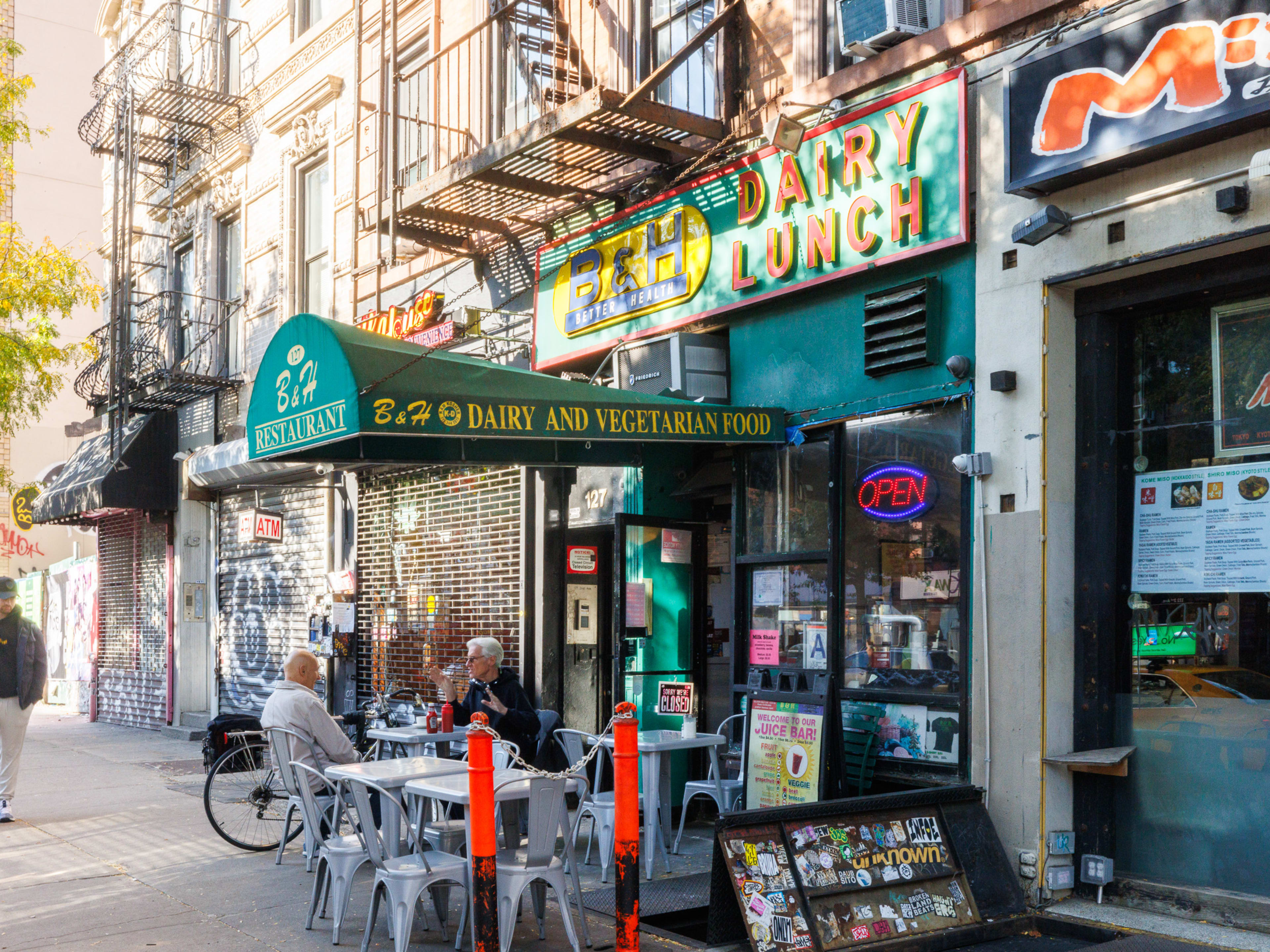 B&H Dairy exterior with metal outdoor tables and an awning