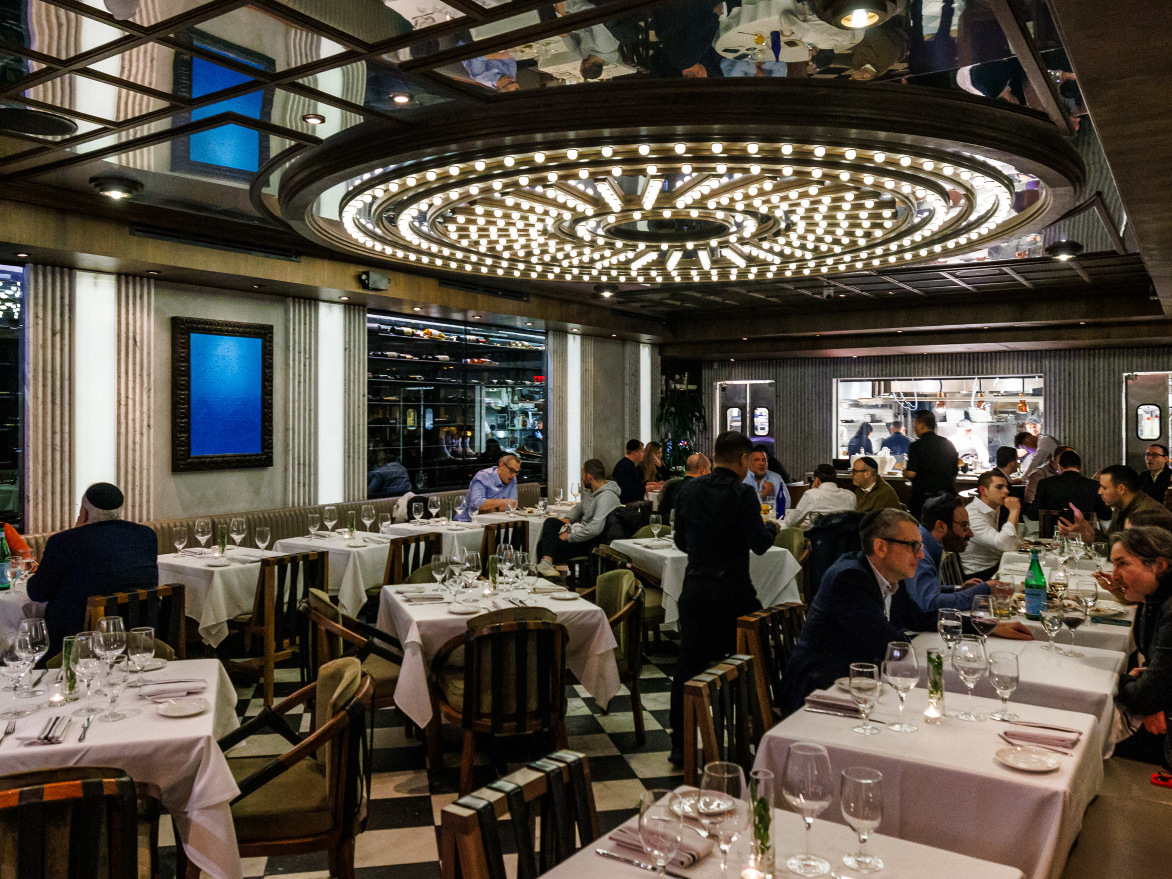 Barnea Bistro interiors with a large circular light fixture on the ceiling and people dining at square tables with white table cloths