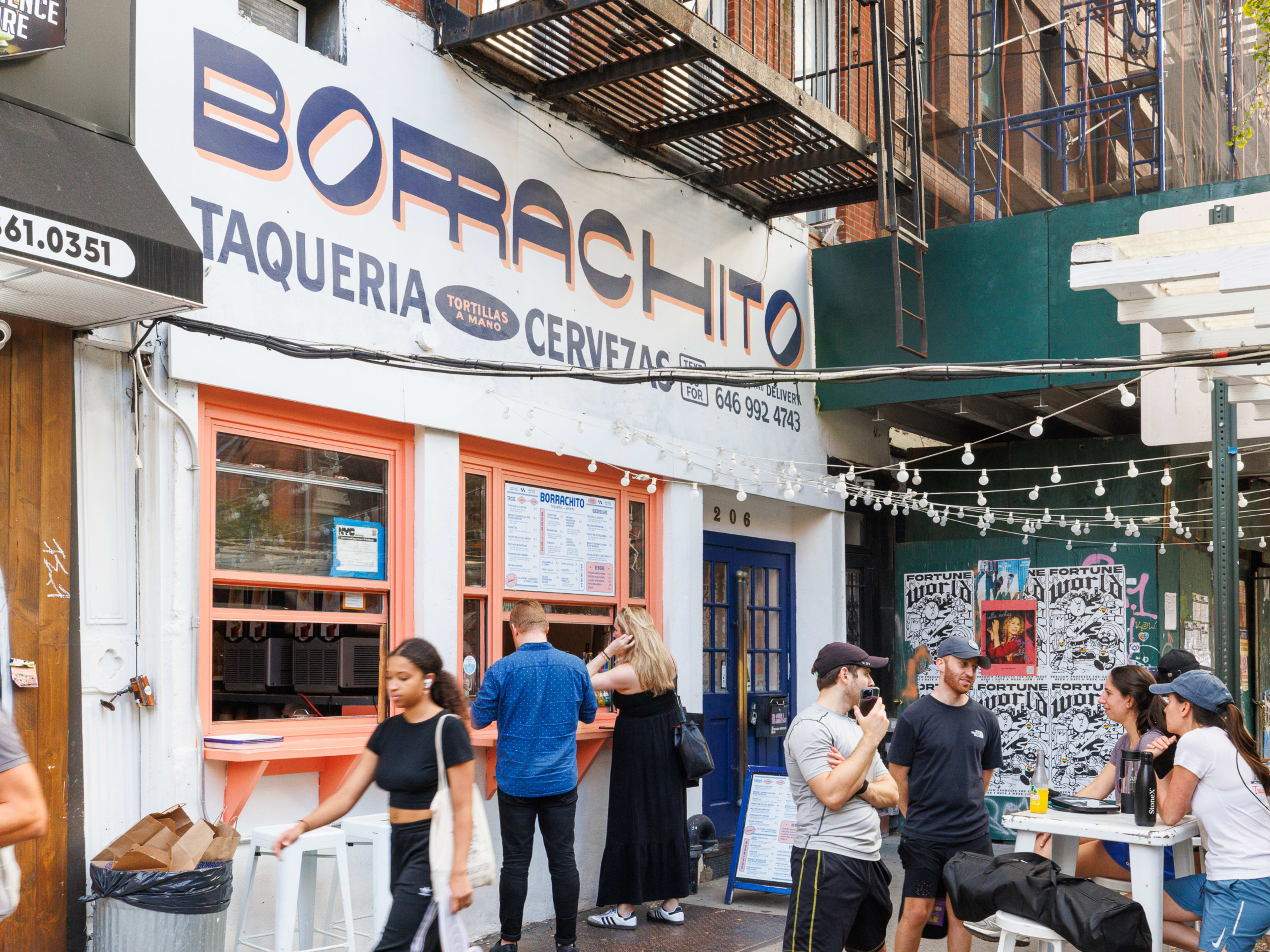 Borrachito exterior with people ordering from a takeout window and standing around high top table seating on the sidewalk out front