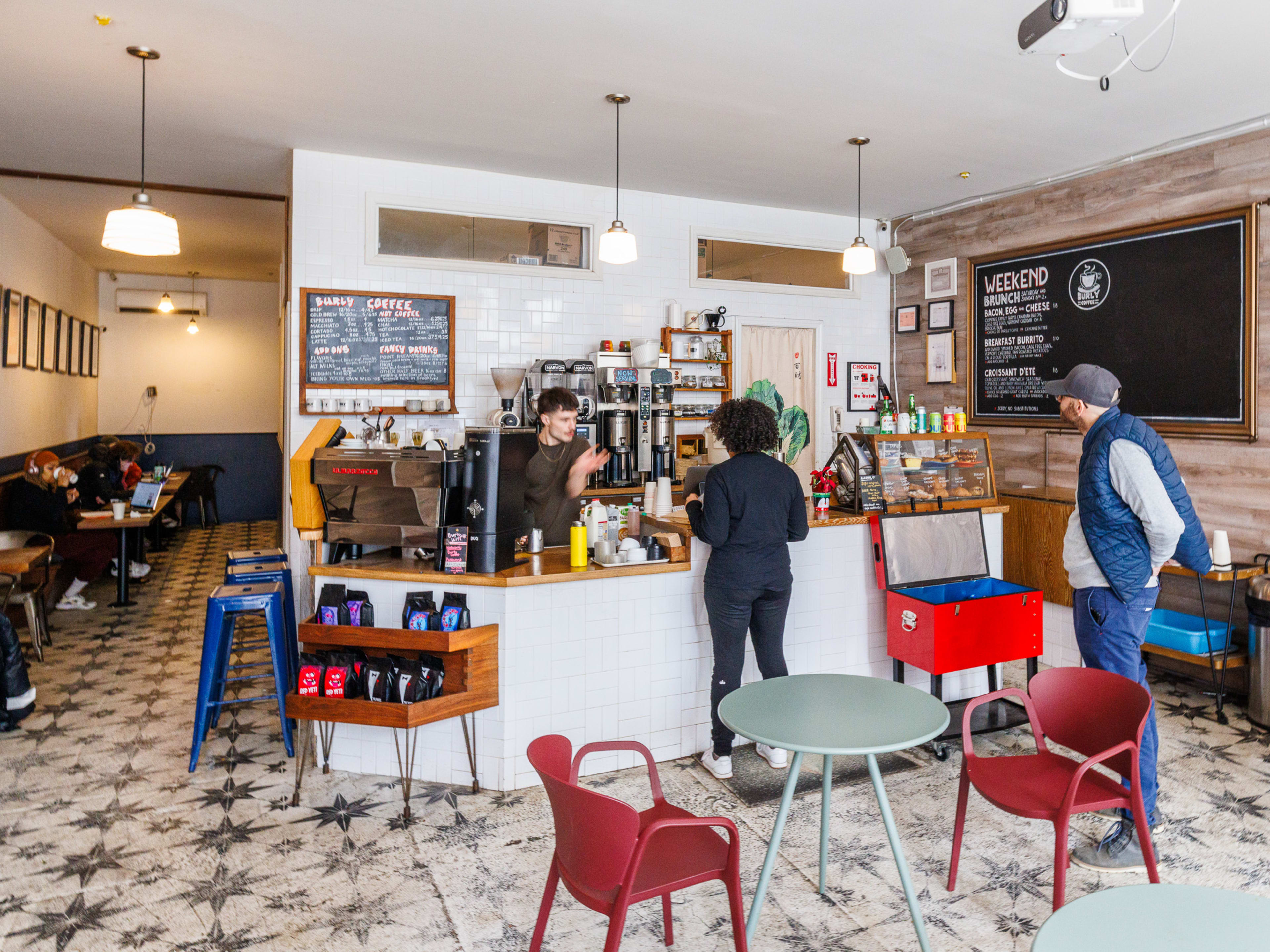 Burly Coffee interior with colorful tables, people ordering at the counter, and a chalkboard menu