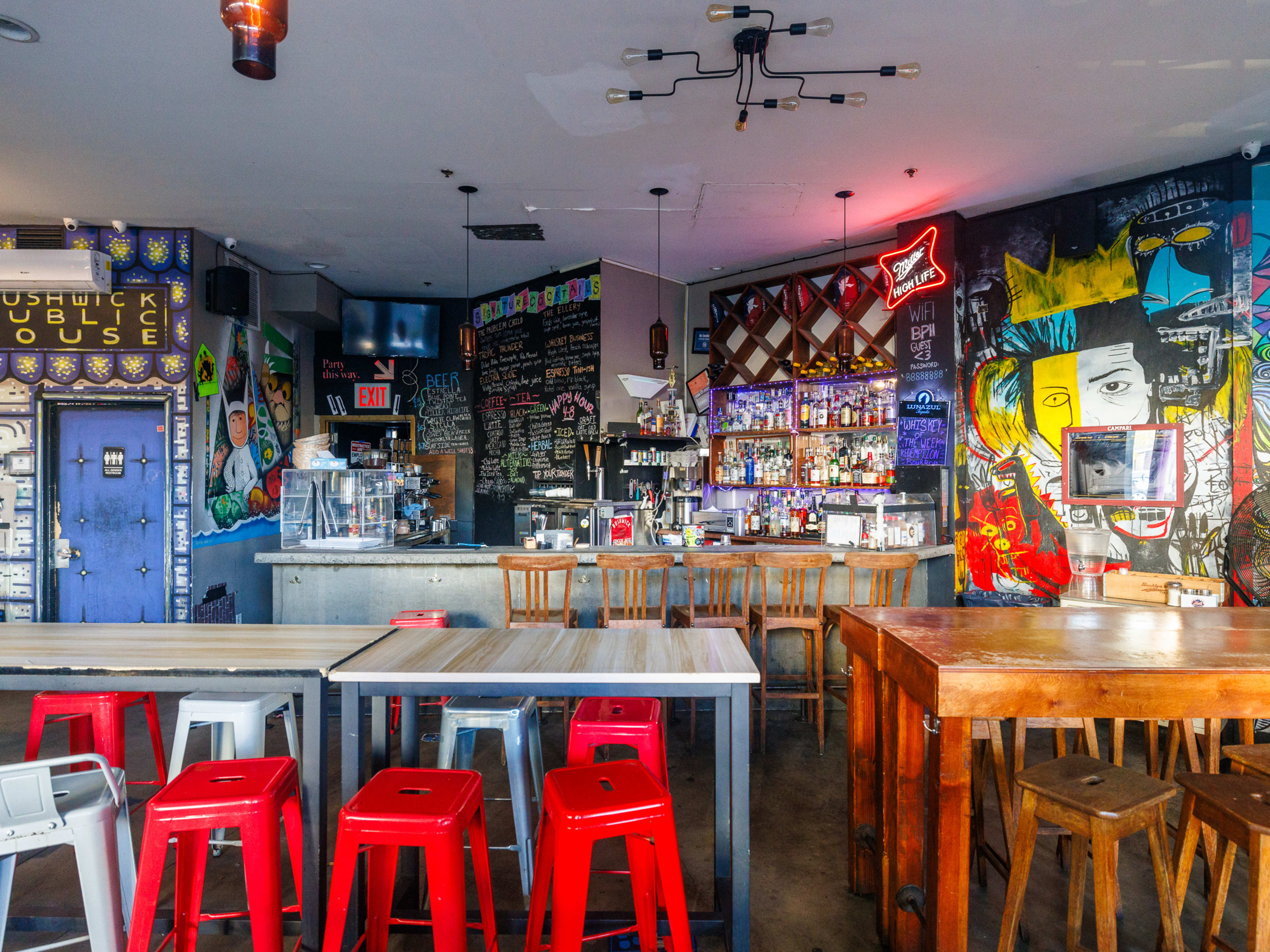 Bushwick Public House interior with stool seating, painted murals on the walls, and neon signs