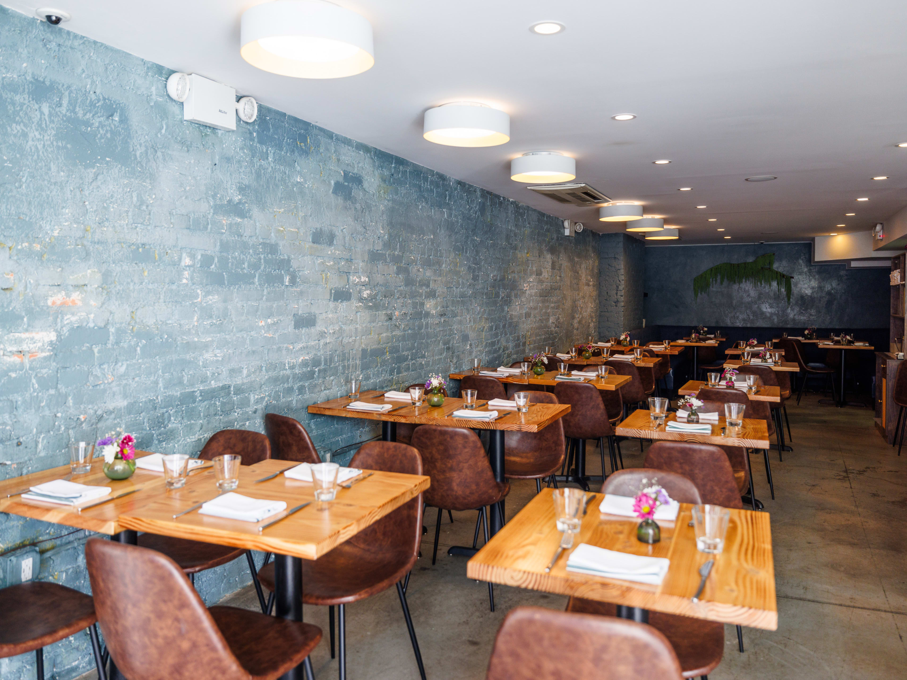 Candle Cafe interiors with blue gray brick walls and square wooden tables set with place settings