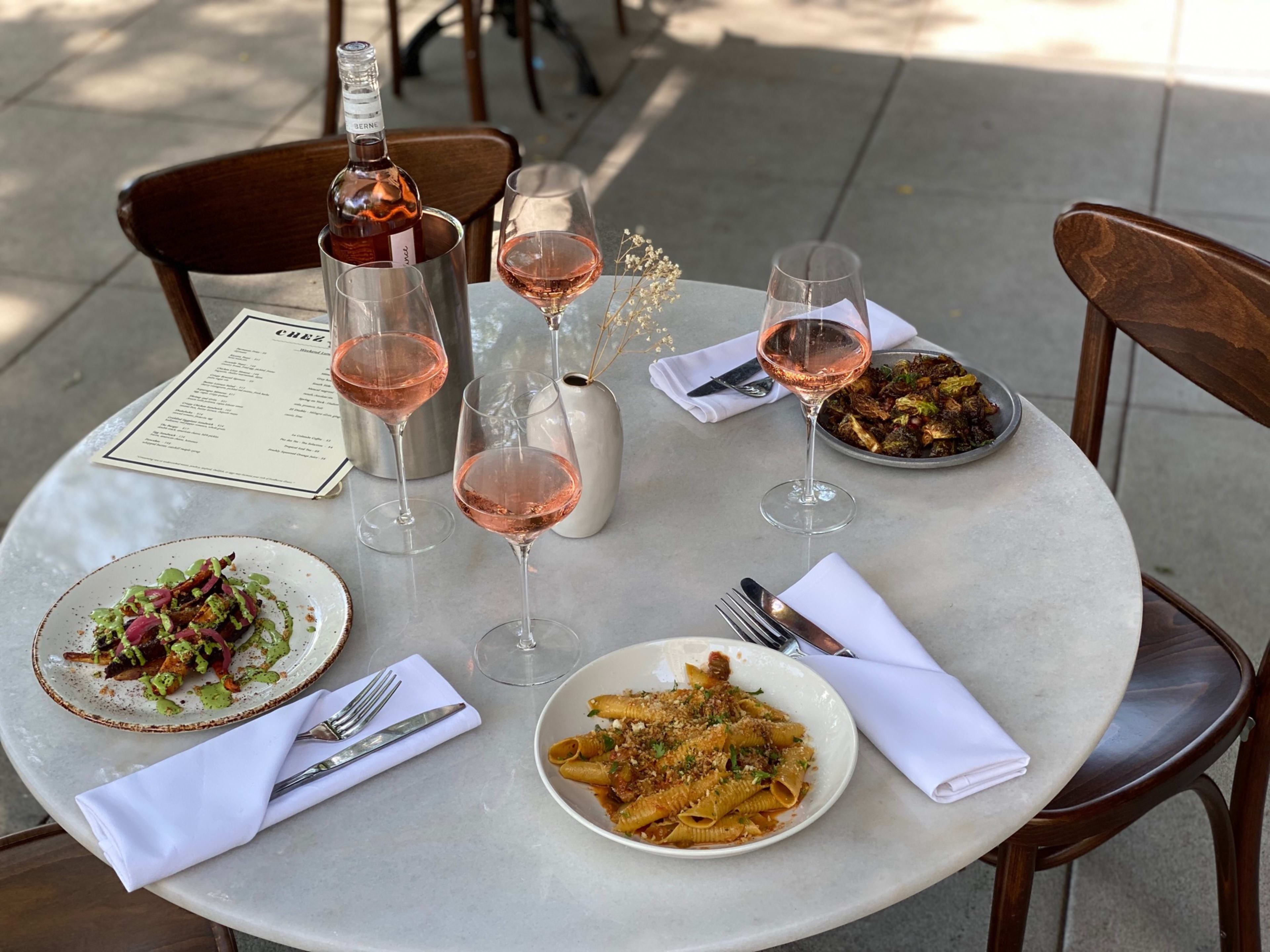 Outdoor dining food spread with pasta and rosé wine on a marble table at Chez Nick