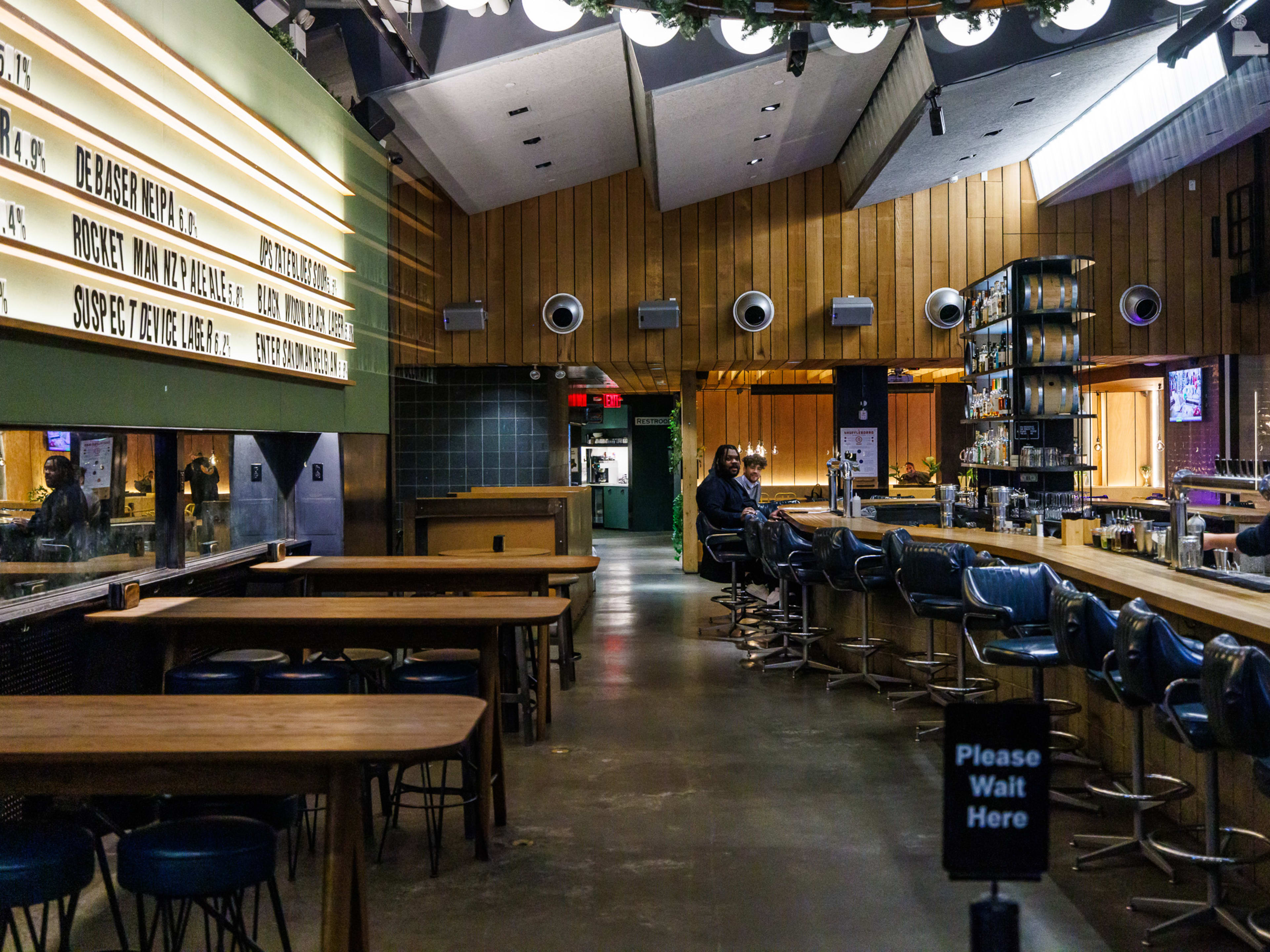 Circa Brewing Co interior with a large marquee drink menu on the left, high top stool seating, bar seating, and wood paneled walls