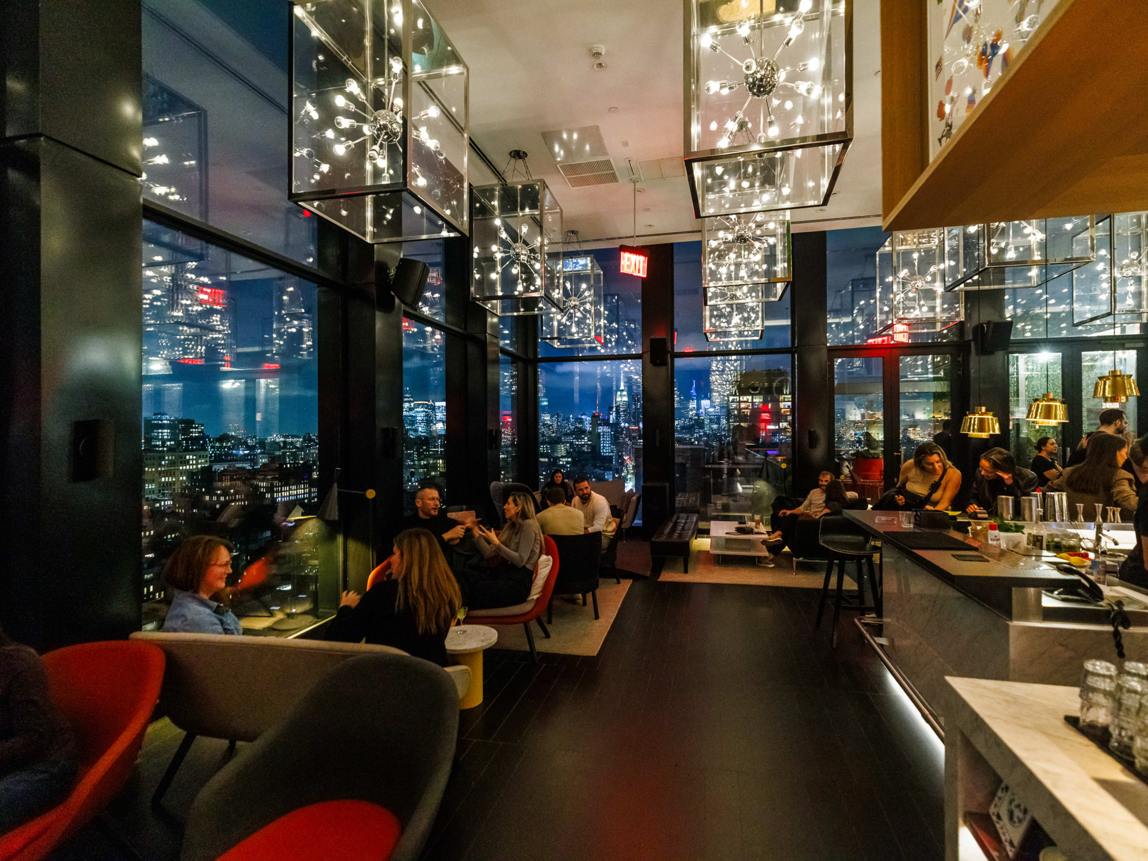 CloudM Rooftop Bar interiors with multiple silver modern light fixtures hanging from the ceiling and guests seated in lounge chairs and couches around the bar